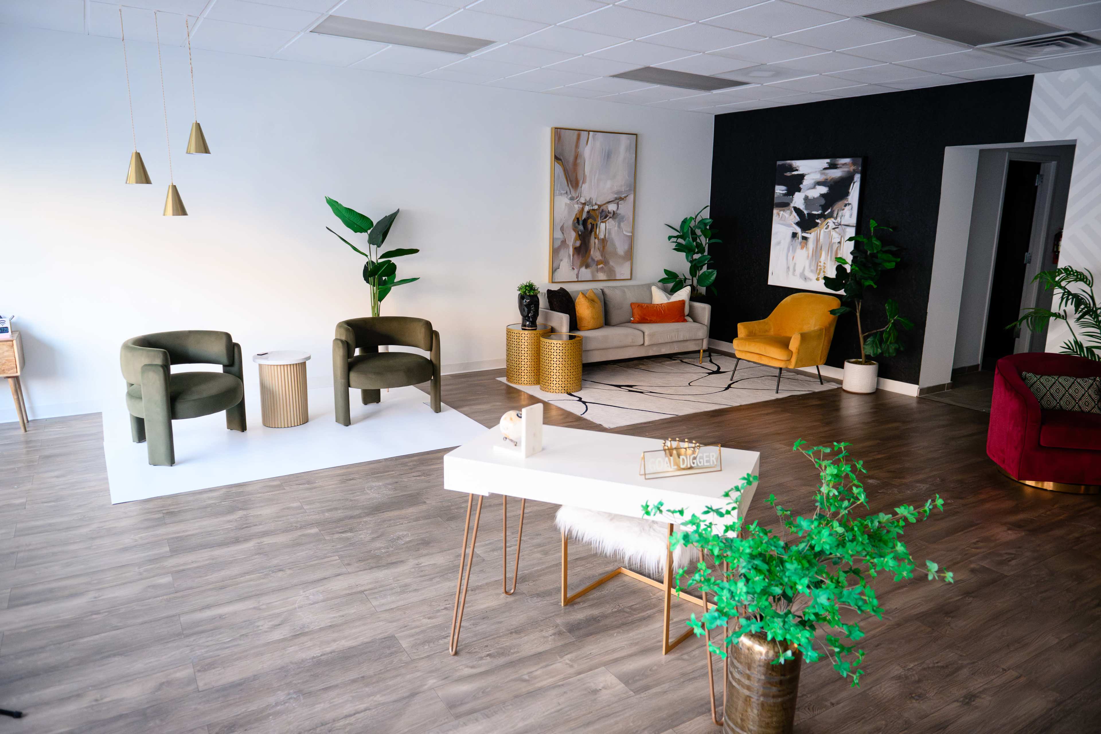 The image depicts a spacious, modern room featuring a mix of seating areas, including green and yellow chairs, a sofa, and various decorative plants.