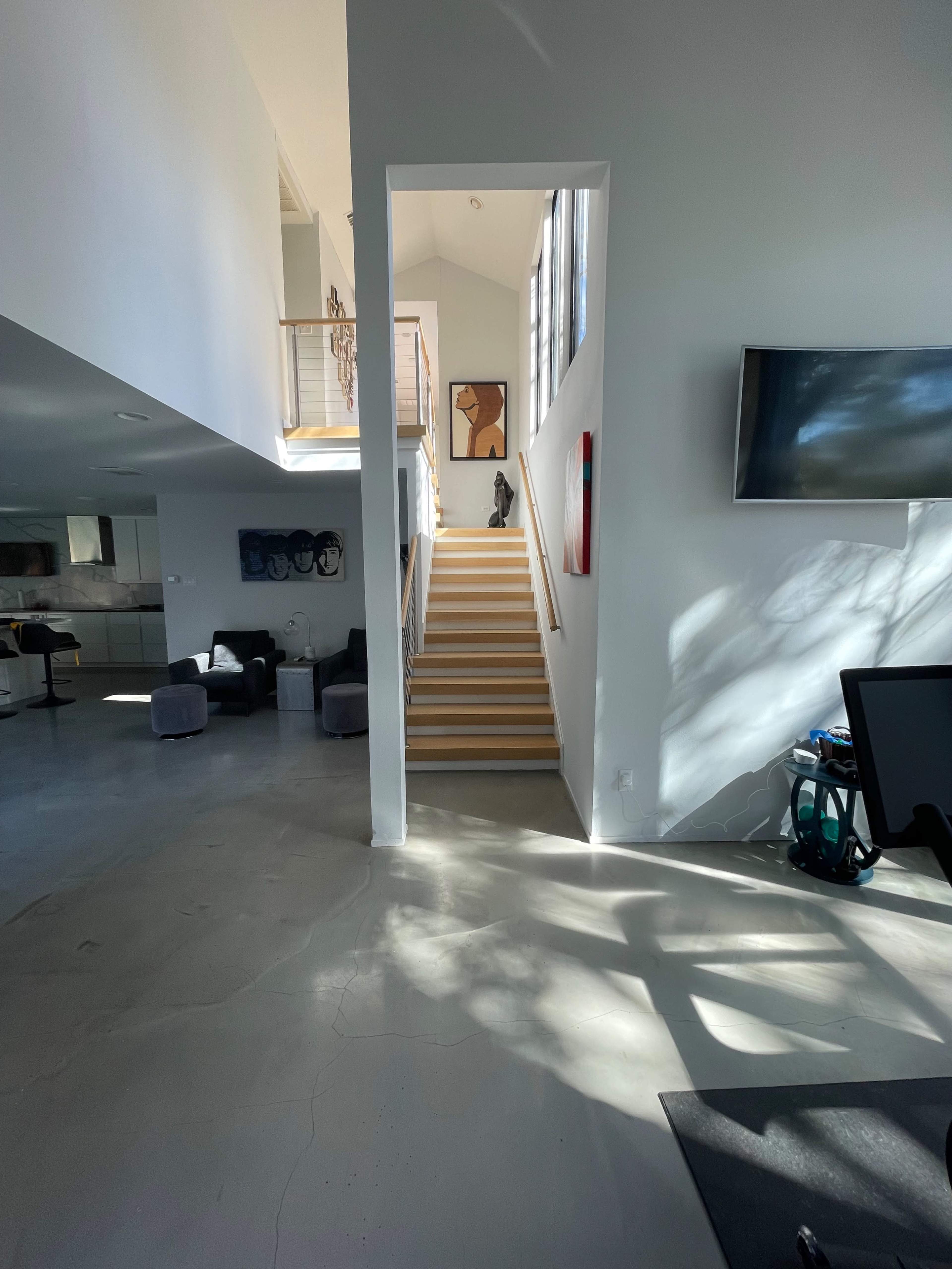 A bright interior space features a staircase leading to an upper level, with minimalist furniture and large windows allowing natural light to fill the area.