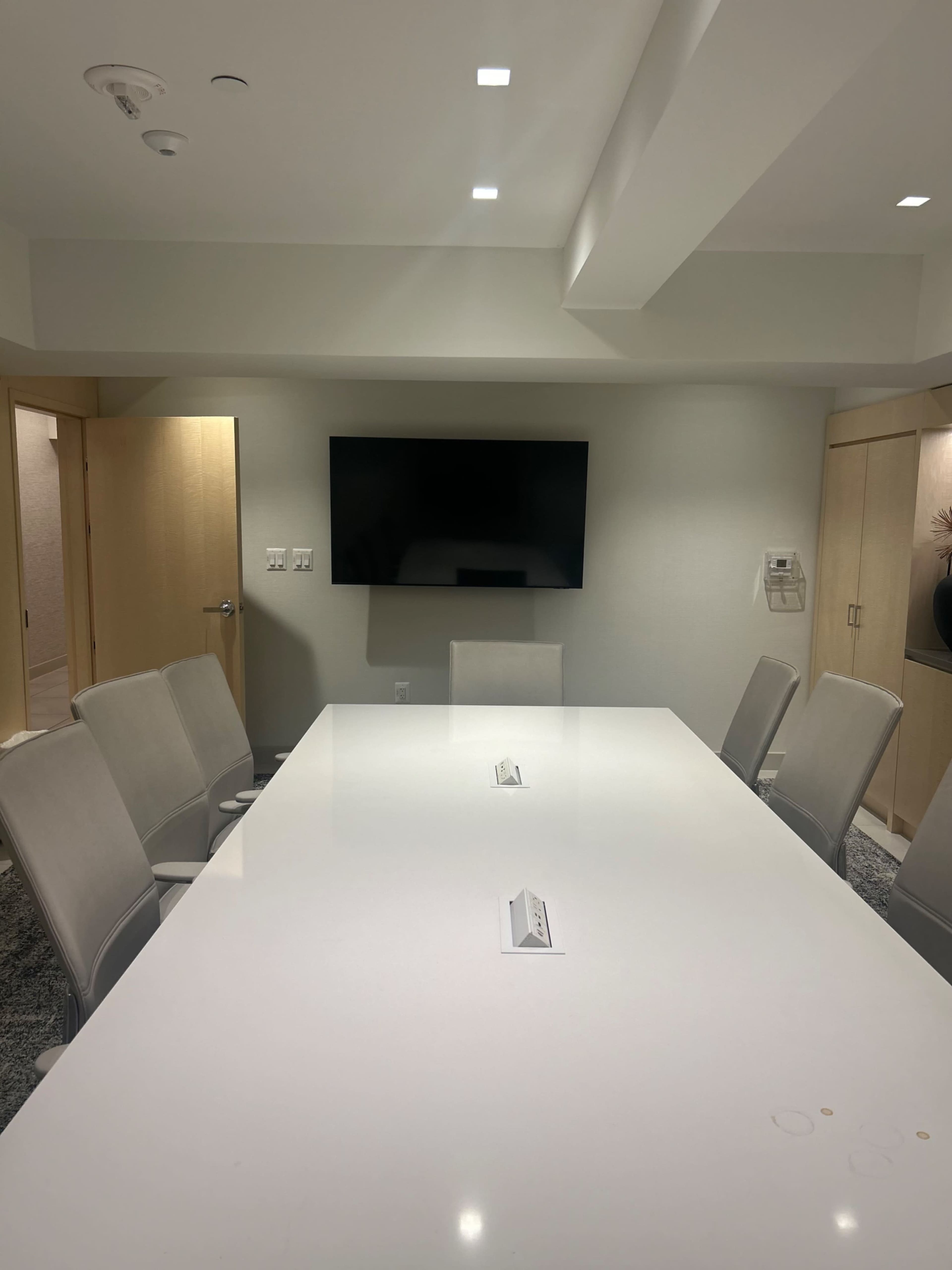 The image shows a modern conference room with a large white table, several chairs, and a wall-mounted television.
