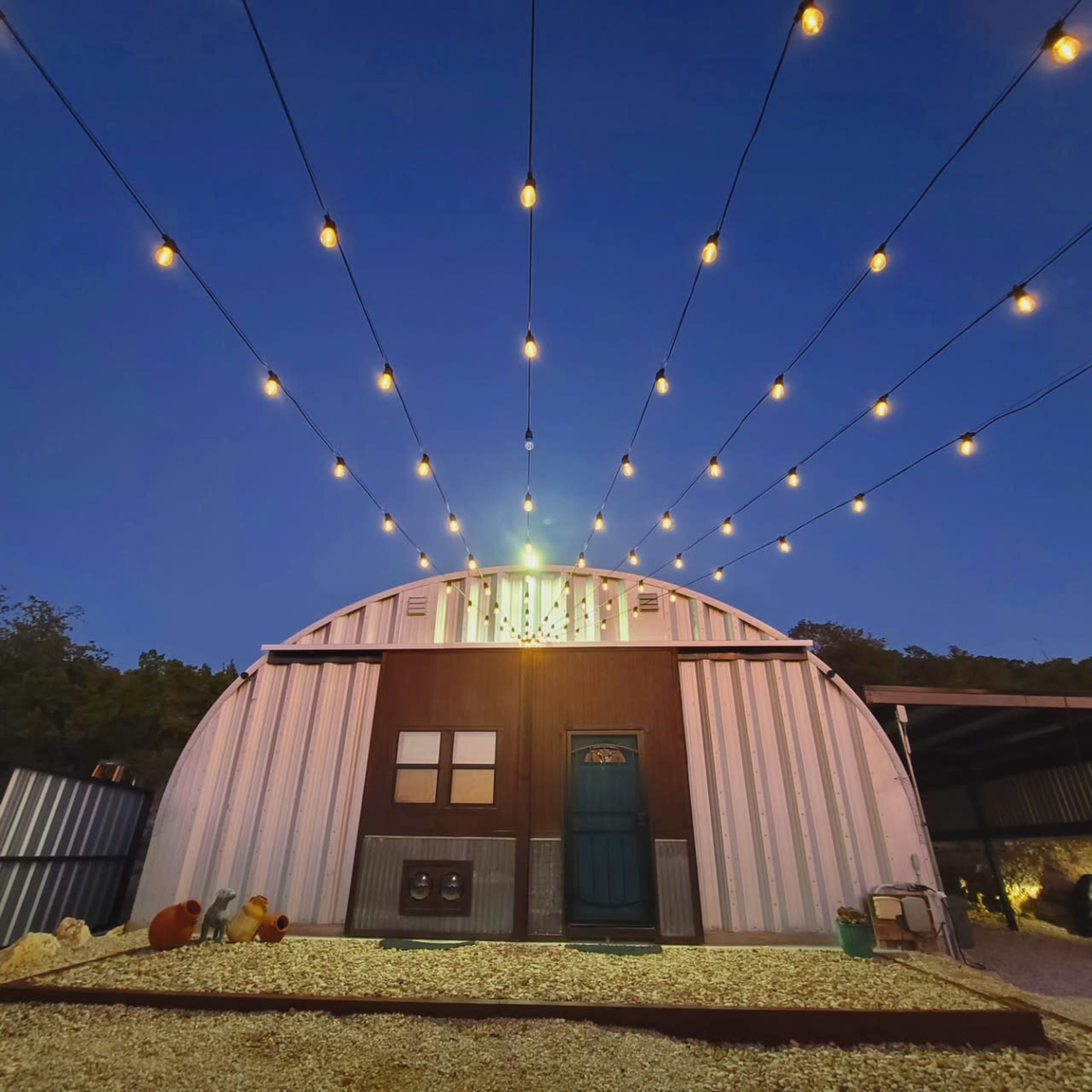 A metal building is illuminated by string lights against a twilight sky.