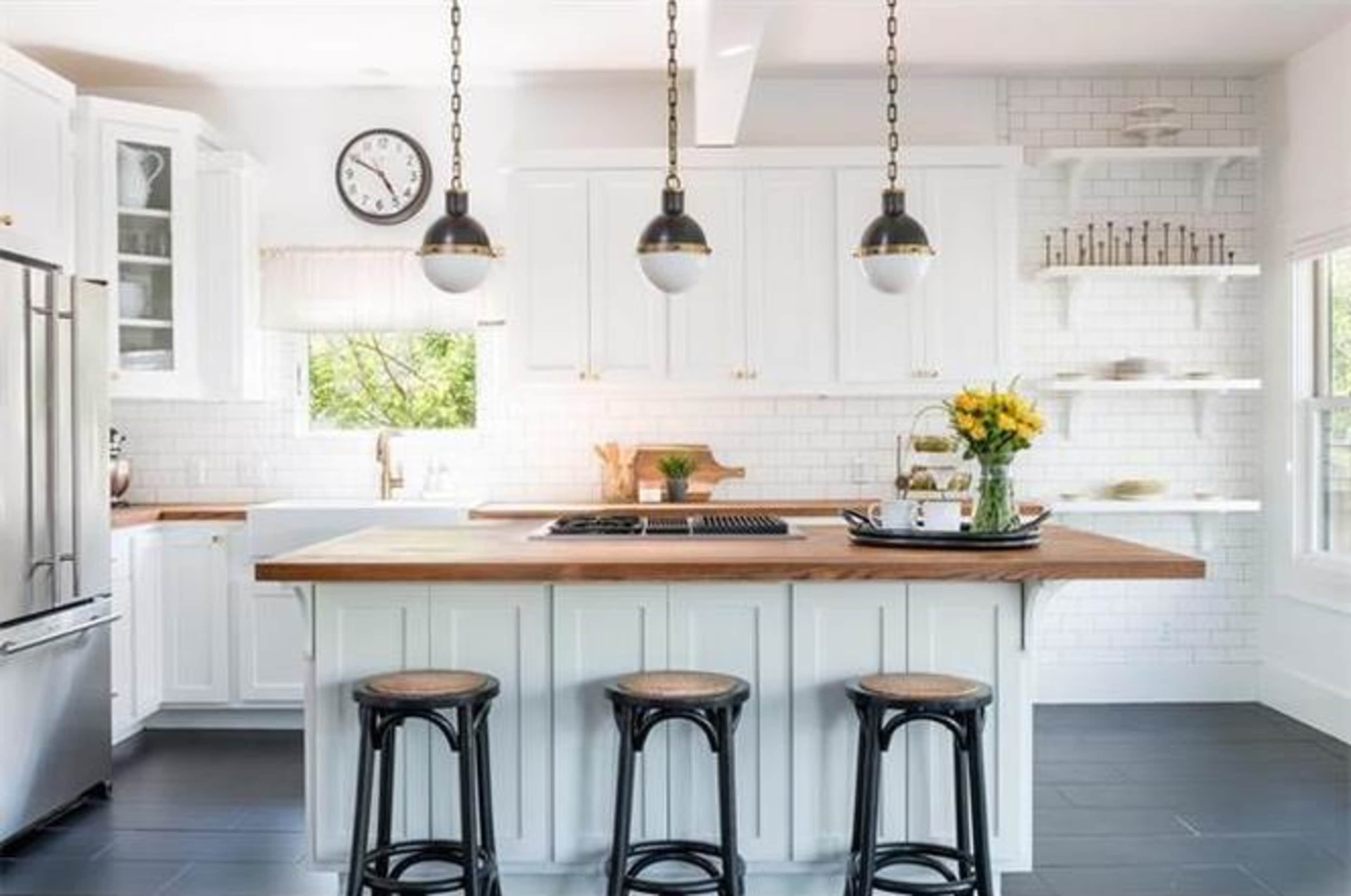 A modern kitchen features white cabinetry, a wooden island with bar stools, and pendant lights above.