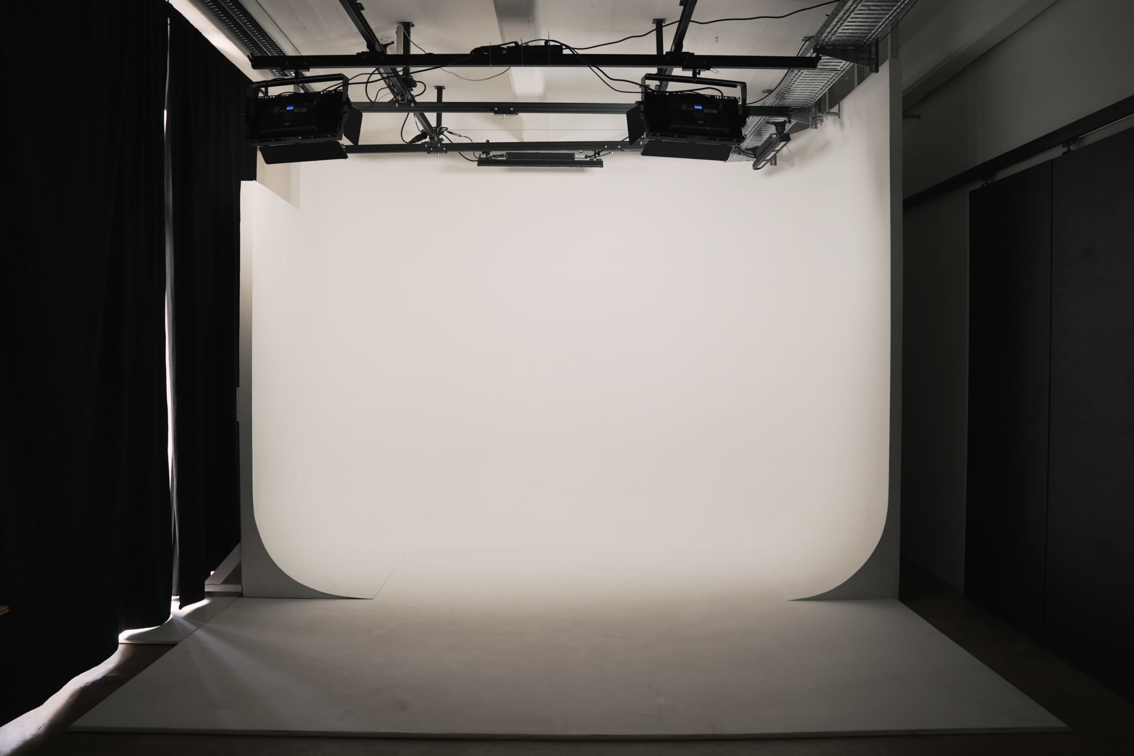 The image shows a minimalist photography studio with a seamless white backdrop and lighting equipment overhead.