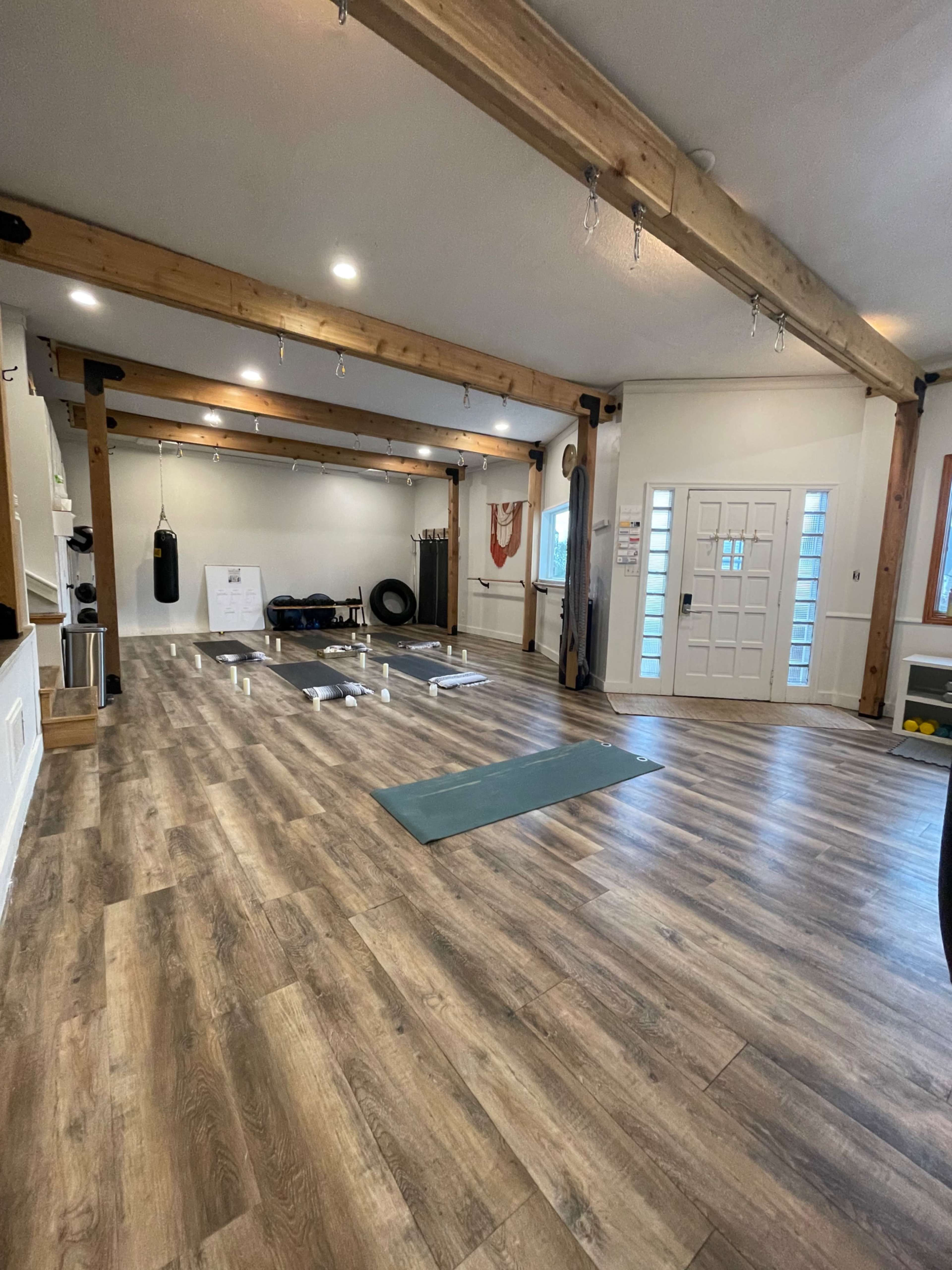 A fitness studio with wooden beams, mats on the floor, a punching bag, and a large entrance door.