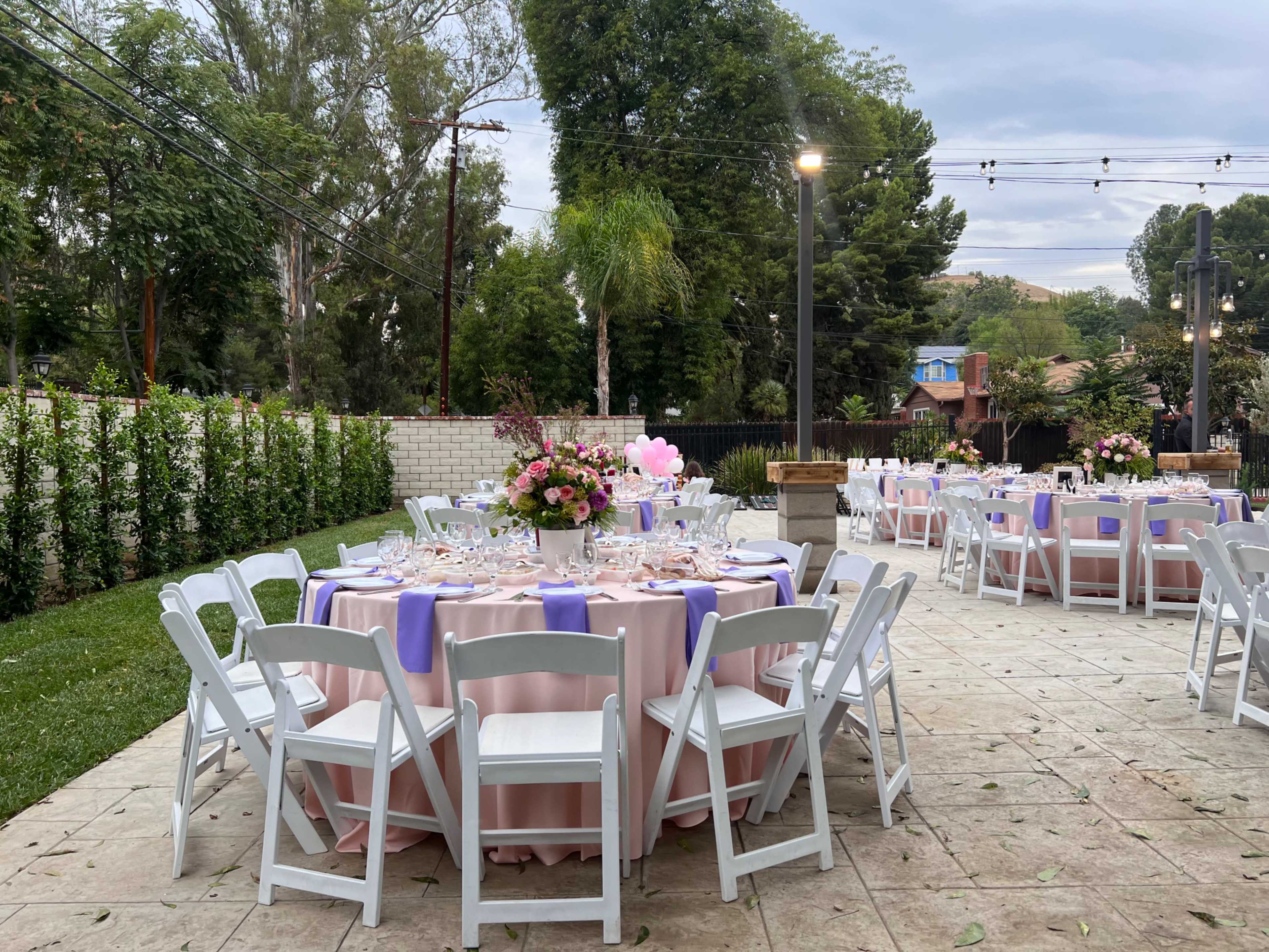 The scene features an outdoor dining area with round tables set for a formal event, complete with pink tablecloths and floral centerpieces.