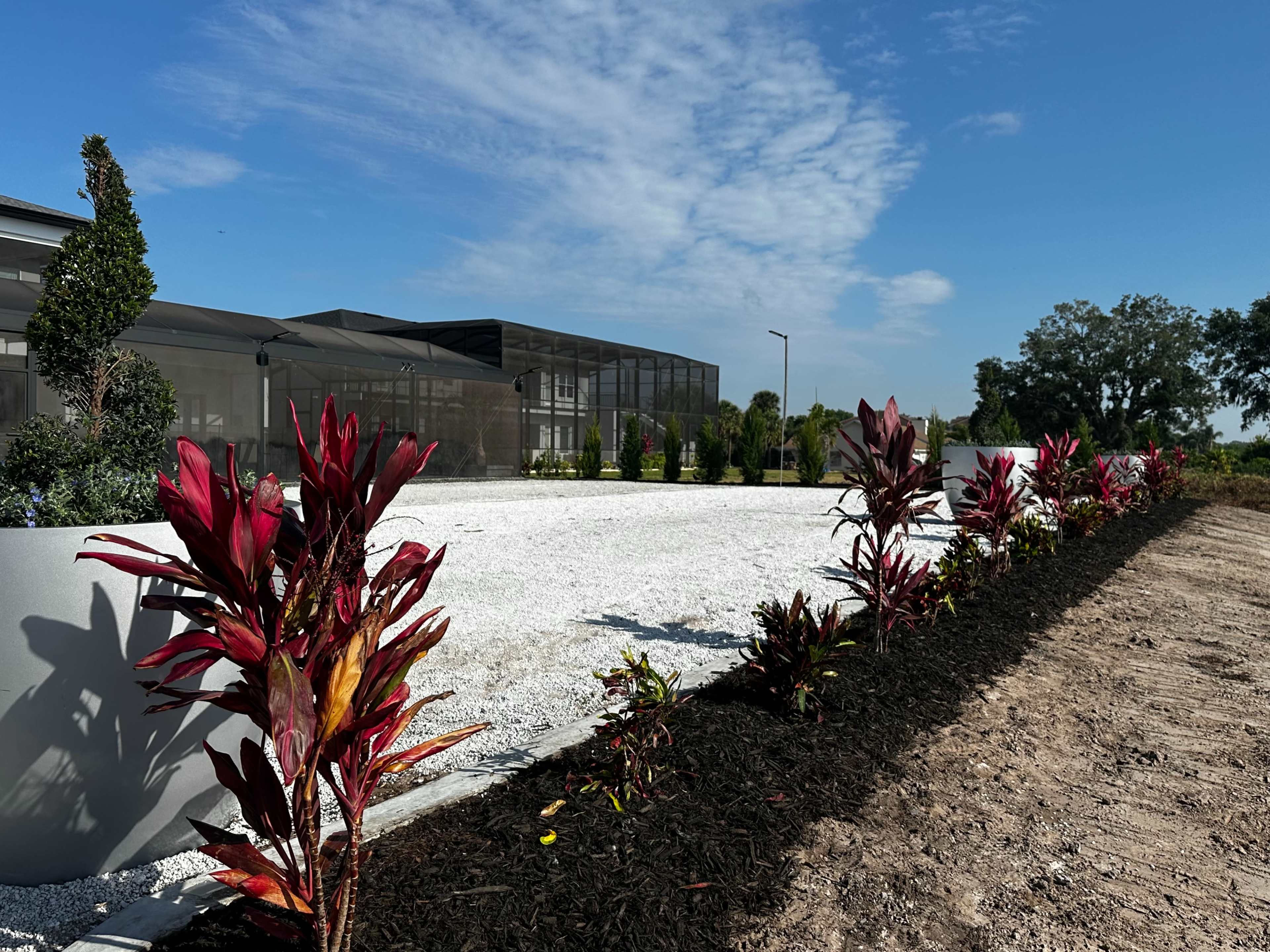 A clean, landscaped area features gravel ground cover and colorful foliage along the edge, with a modern building in the background under a clear blue sky.