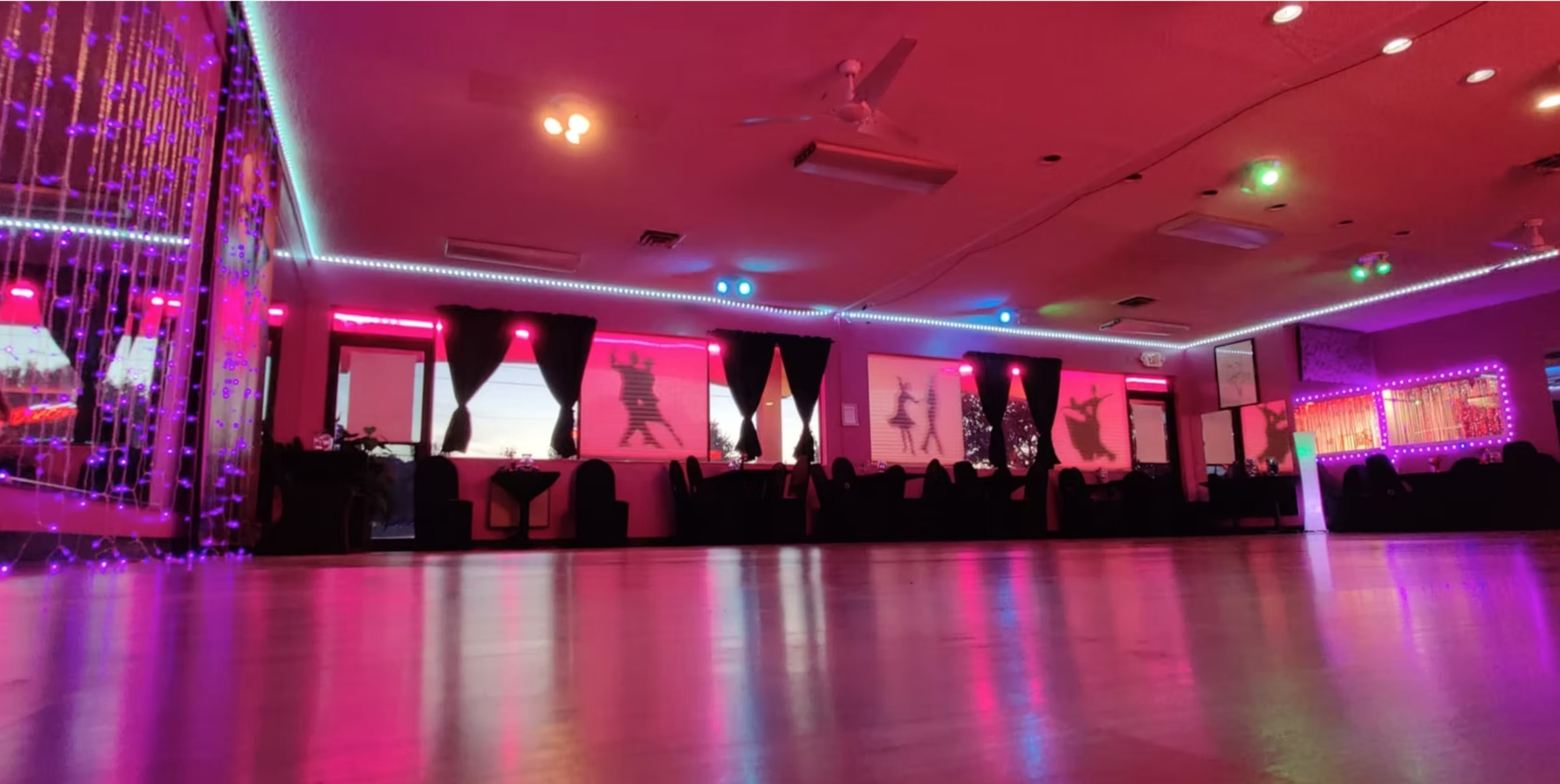 The image shows a dance studio with colorful lighting and shadowed figures projected on the walls.
