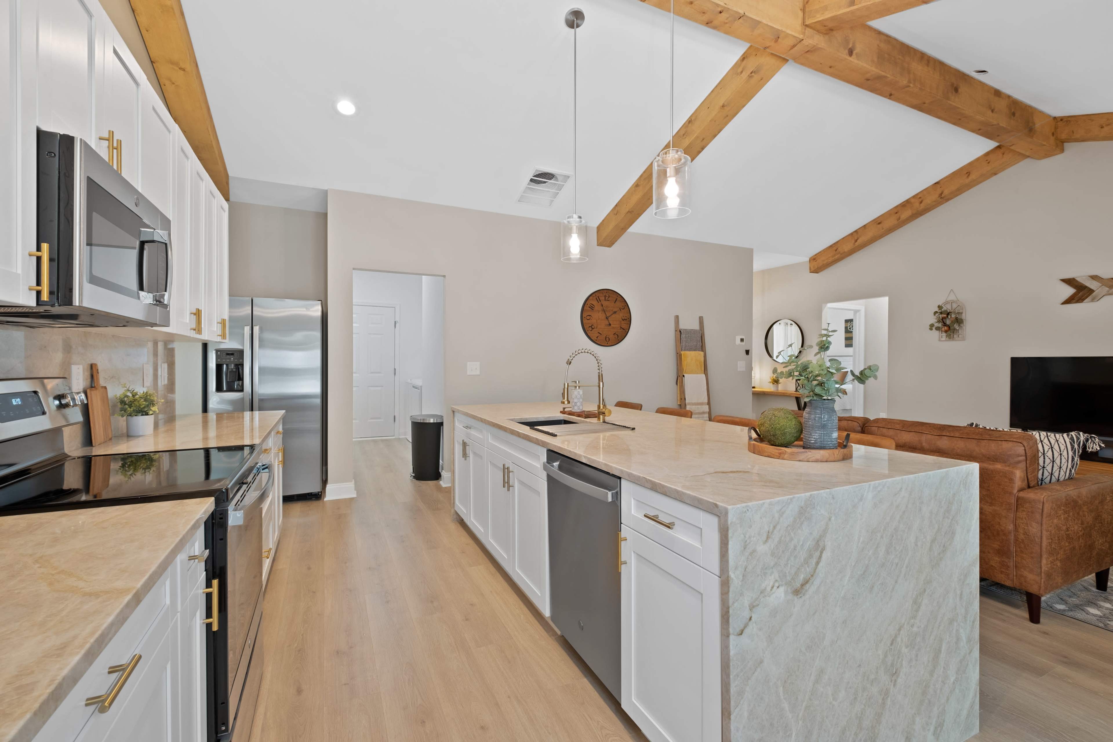 A modern kitchen with white cabinetry, a large island with a marble countertop, stainless steel appliances, and exposed wooden beams on the ceiling.