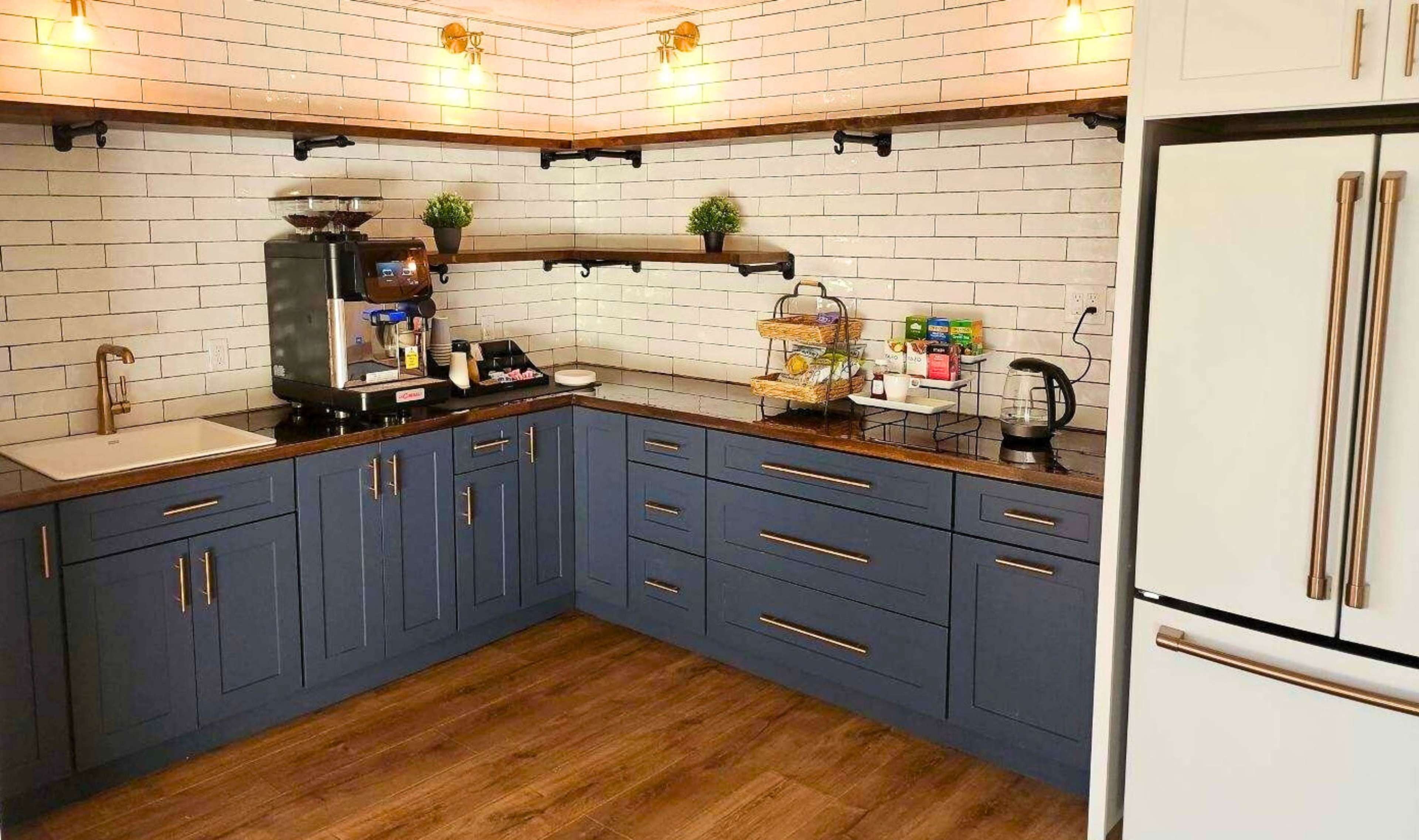 The image shows a modern kitchen with blue cabinets, a coffee station, and a wooden countertop against a white tiled wall.