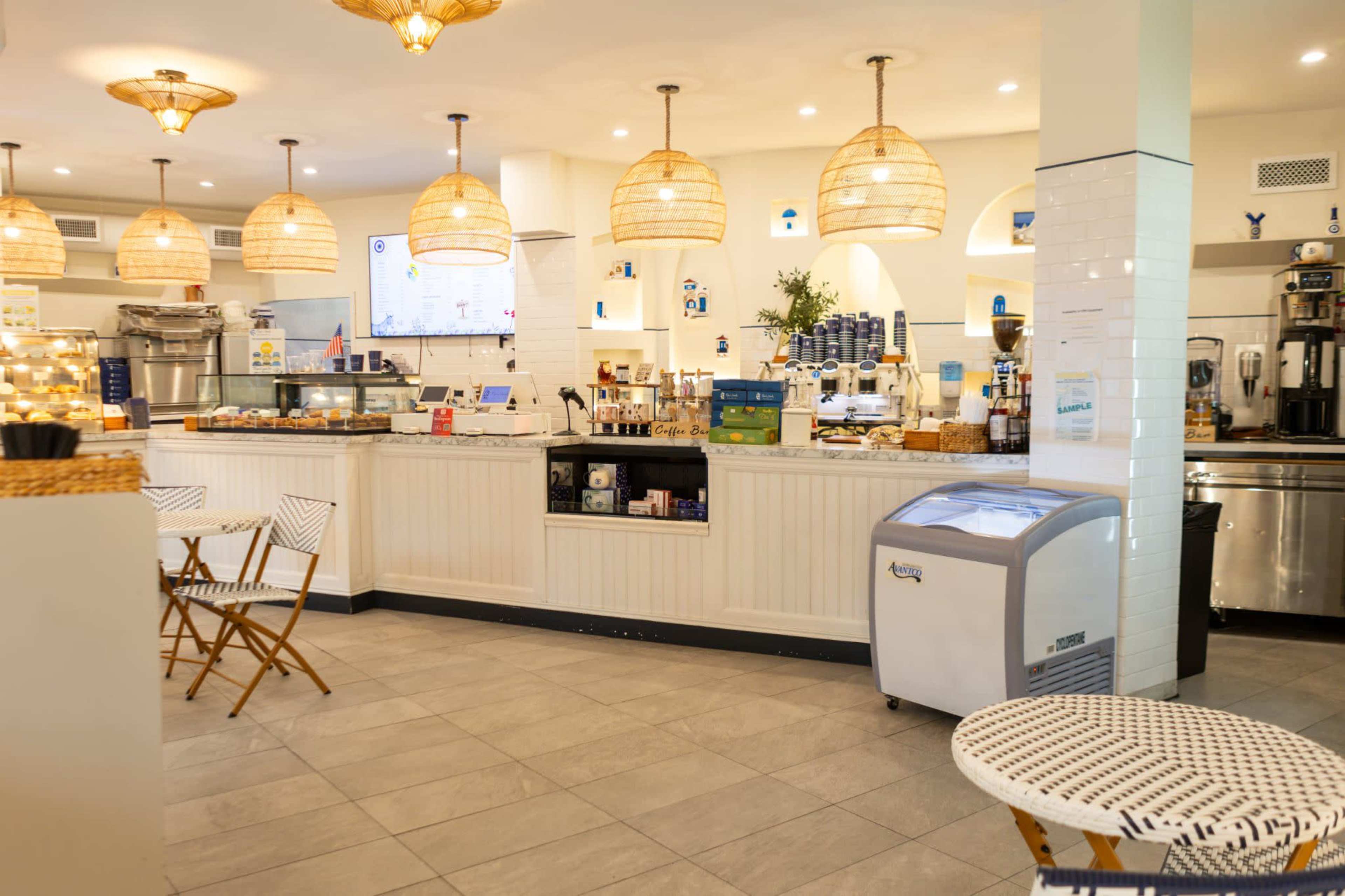 The image shows a brightly lit cafe with a white counter, woven pendant lights, and small bistro tables.