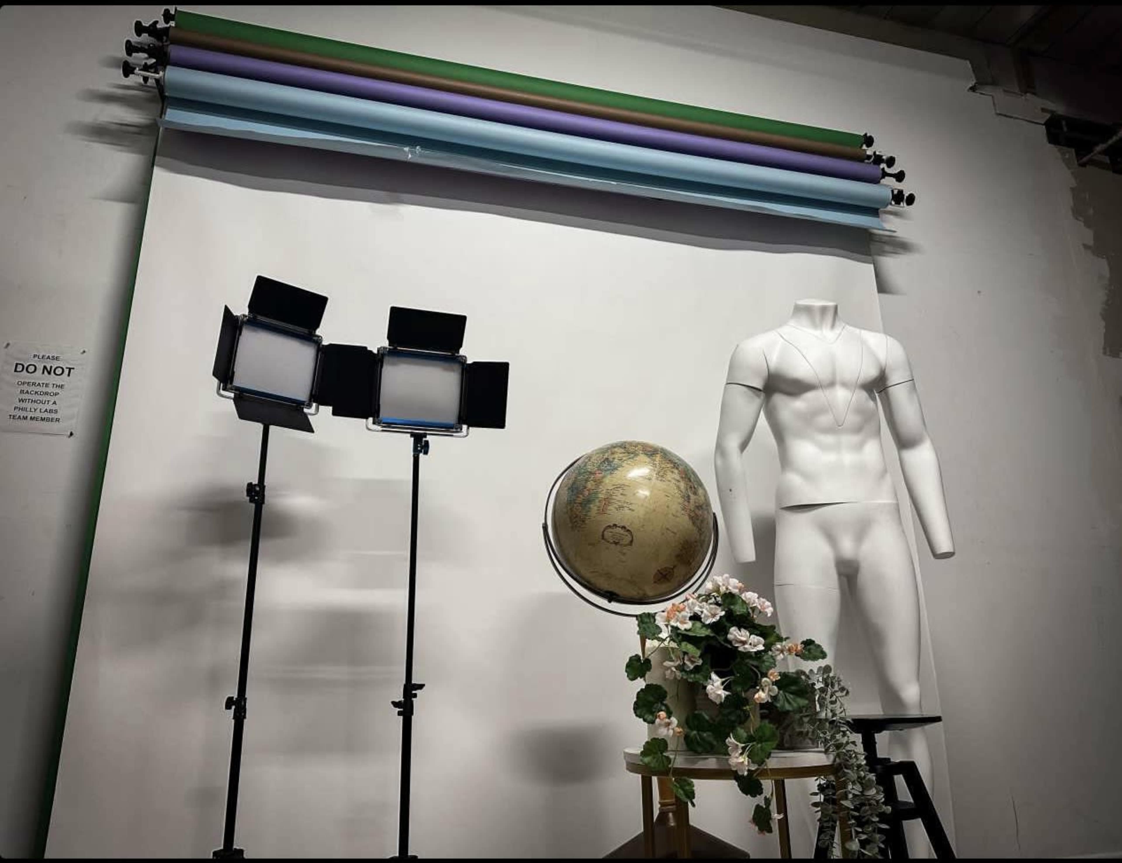 The image features a photography setup with a mannequin, a globe, two light sources, and a backdrop of colorful rolled paper.
