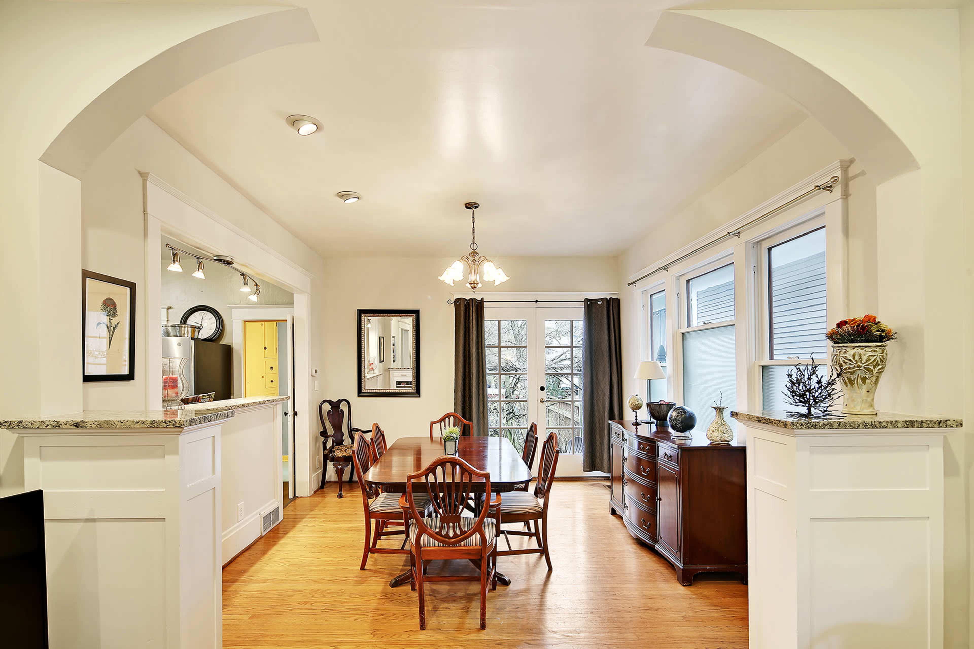 A dining room with a wooden table and chairs, situated next to a window with curtains, and a sideboard against the wall.