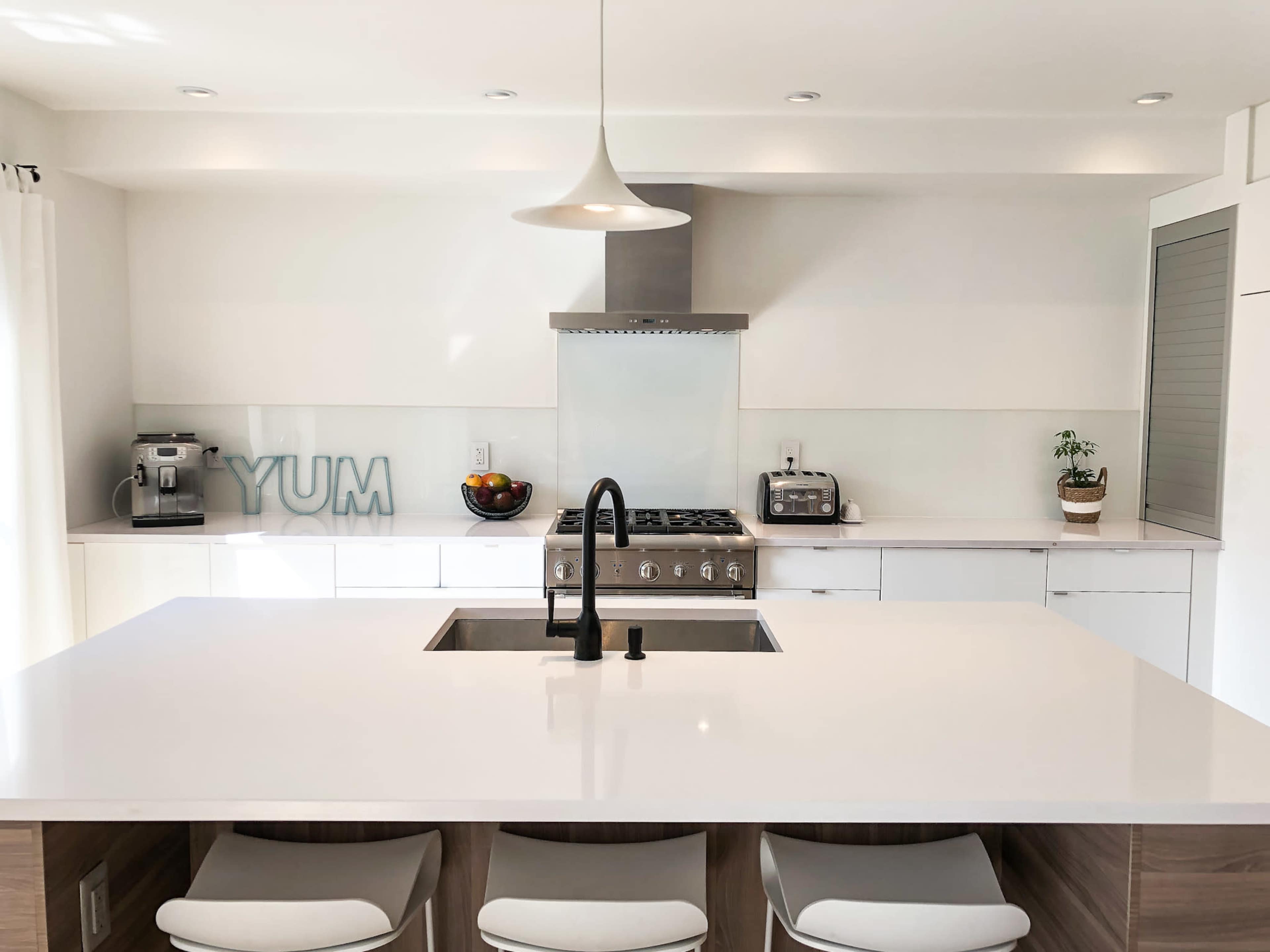 A modern kitchen features a central island with a sink, white countertops, and stainless steel appliances.