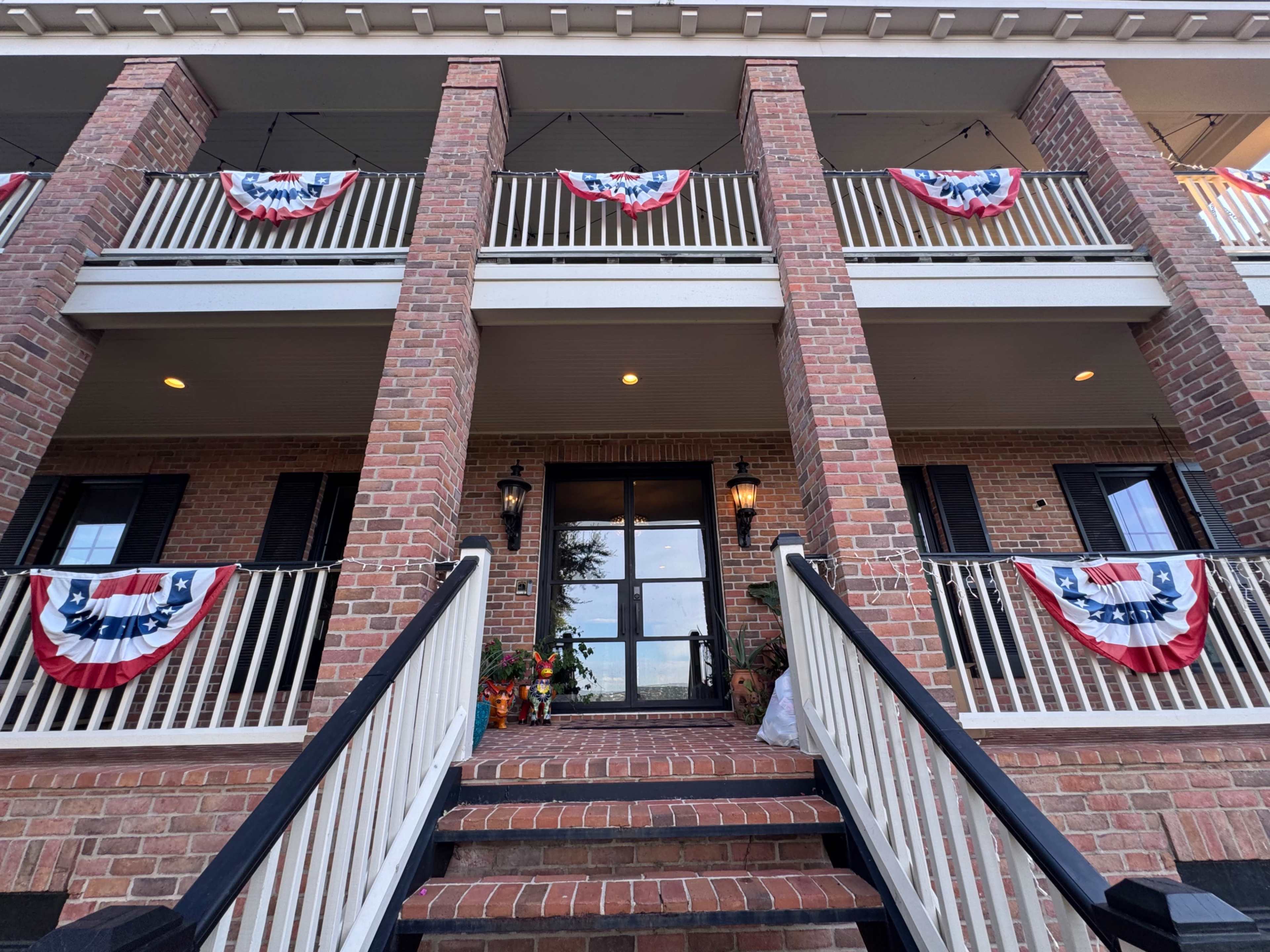 The image shows a brick building with a set of stairs leading to a front door, adorned with red, white, and blue bunting along the balconies.