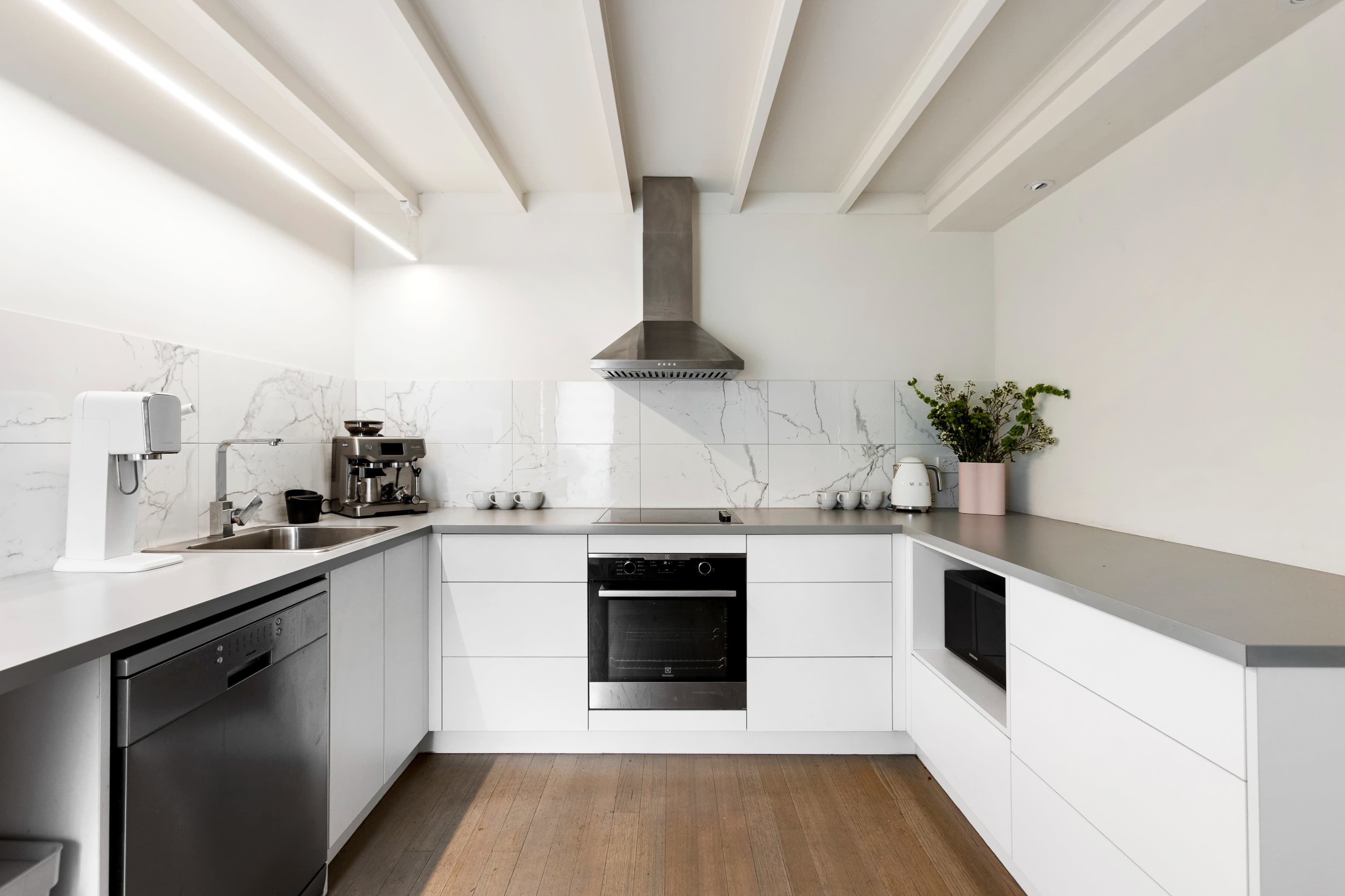 The kitchen features modern white cabinetry, a stainless steel hood over the stove, and a marble backsplash.
