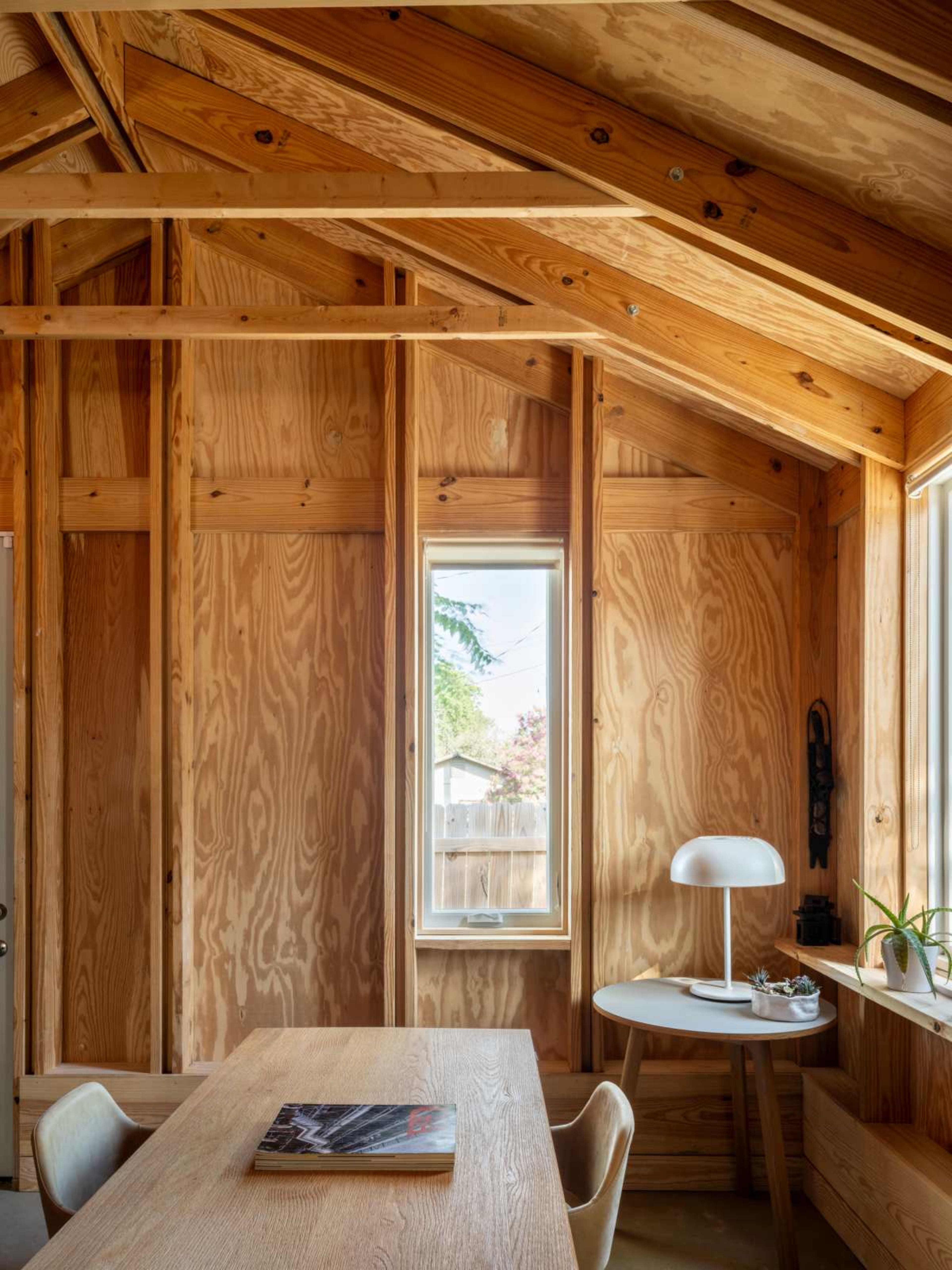 The image shows an interior of a wood-finished room with a table and chairs, framed windows, and a lamp.