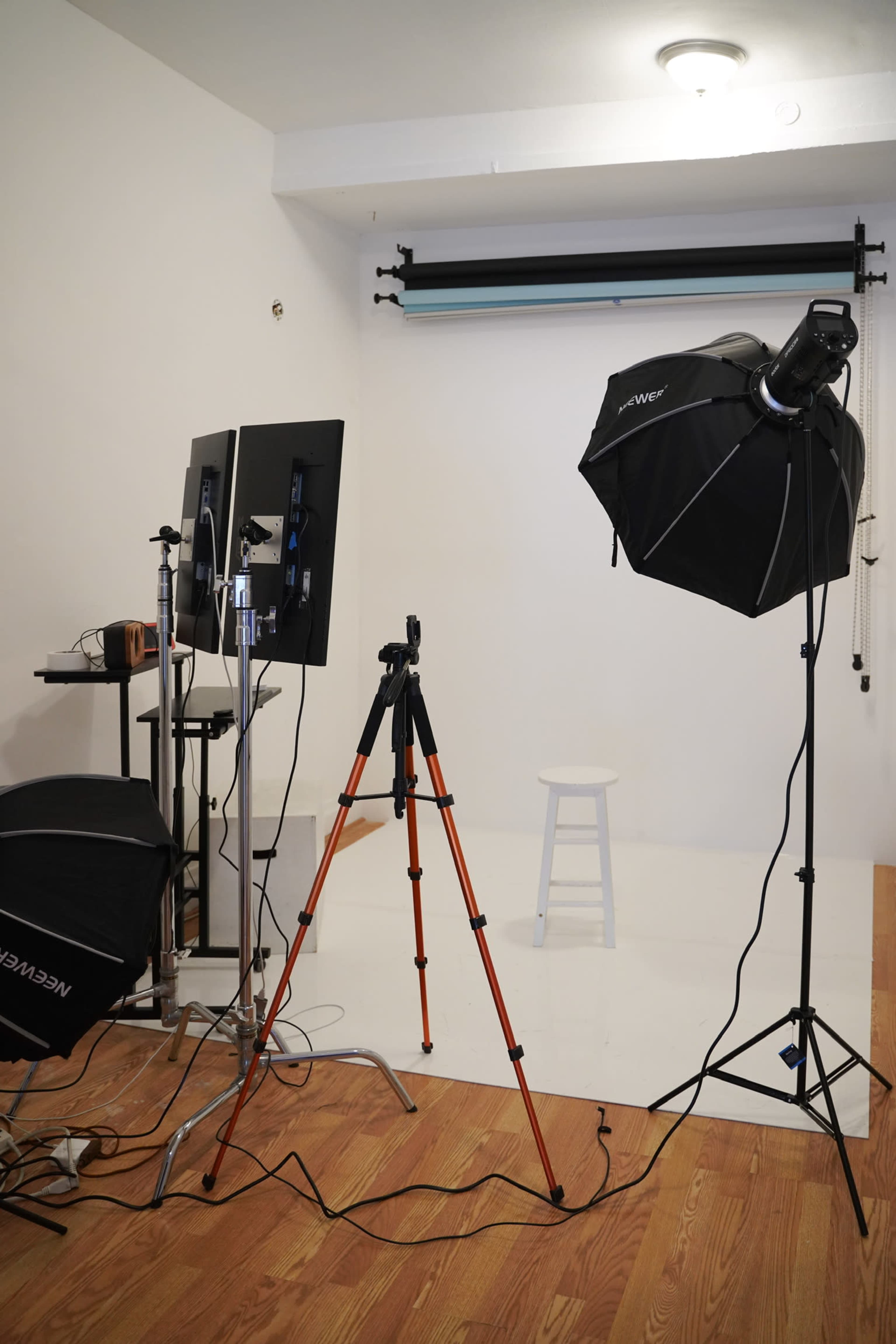 A photography studio with a tripod, lighting equipment, and a white backdrop.