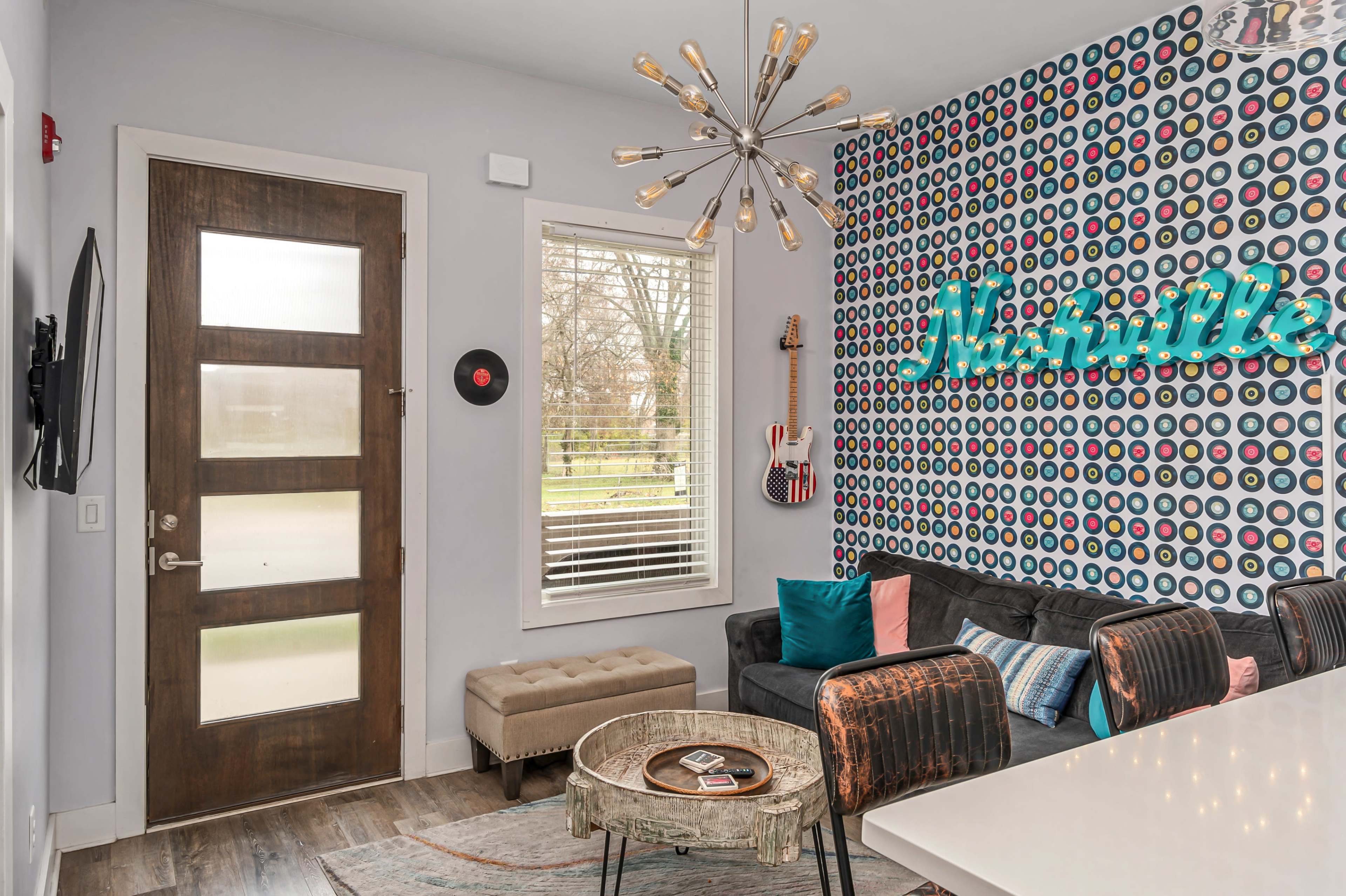 A modern living room with a wooden door, a wall decorated with colorful vinyl records, and a mid-century style sofa next to a round coffee table.