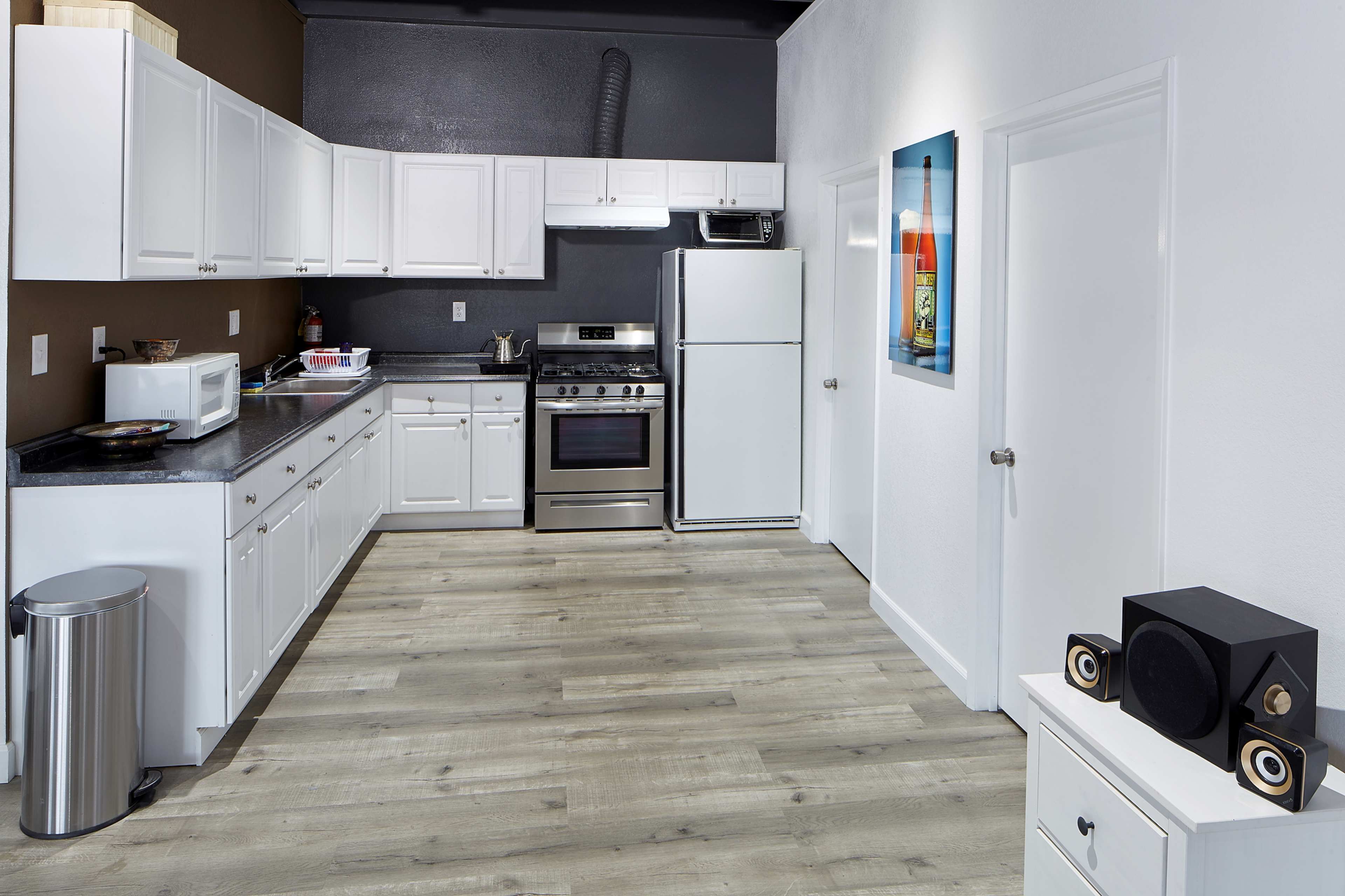 The image shows a modern kitchen with white cabinets, stainless steel appliances, and a light-colored wooden floor.