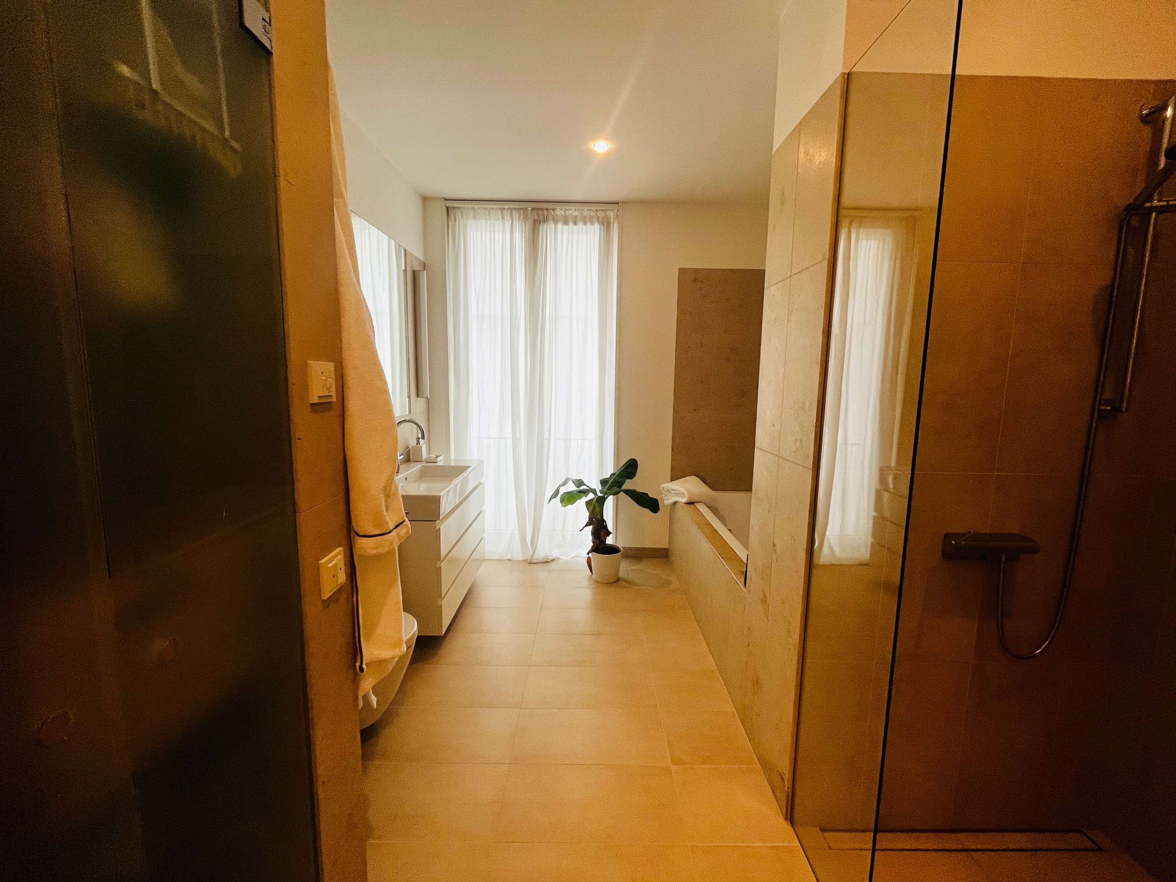 A modern bathroom featuring a glass shower, a bathtub, and large windows with natural light.