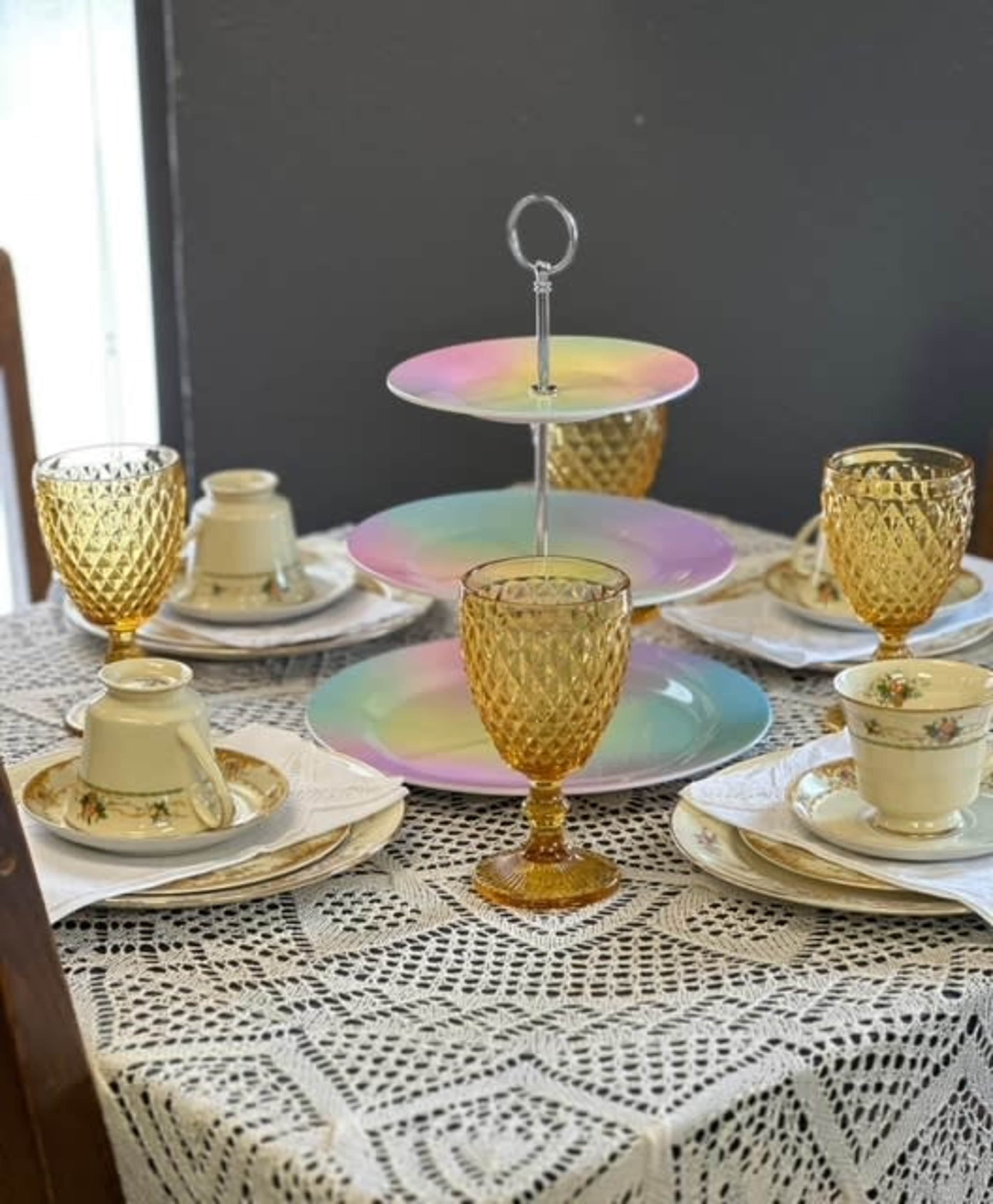 A table is set with an assortment of vintage dishware, including gold-hued goblets, patterned plates, and a multi-tiered serving stand.