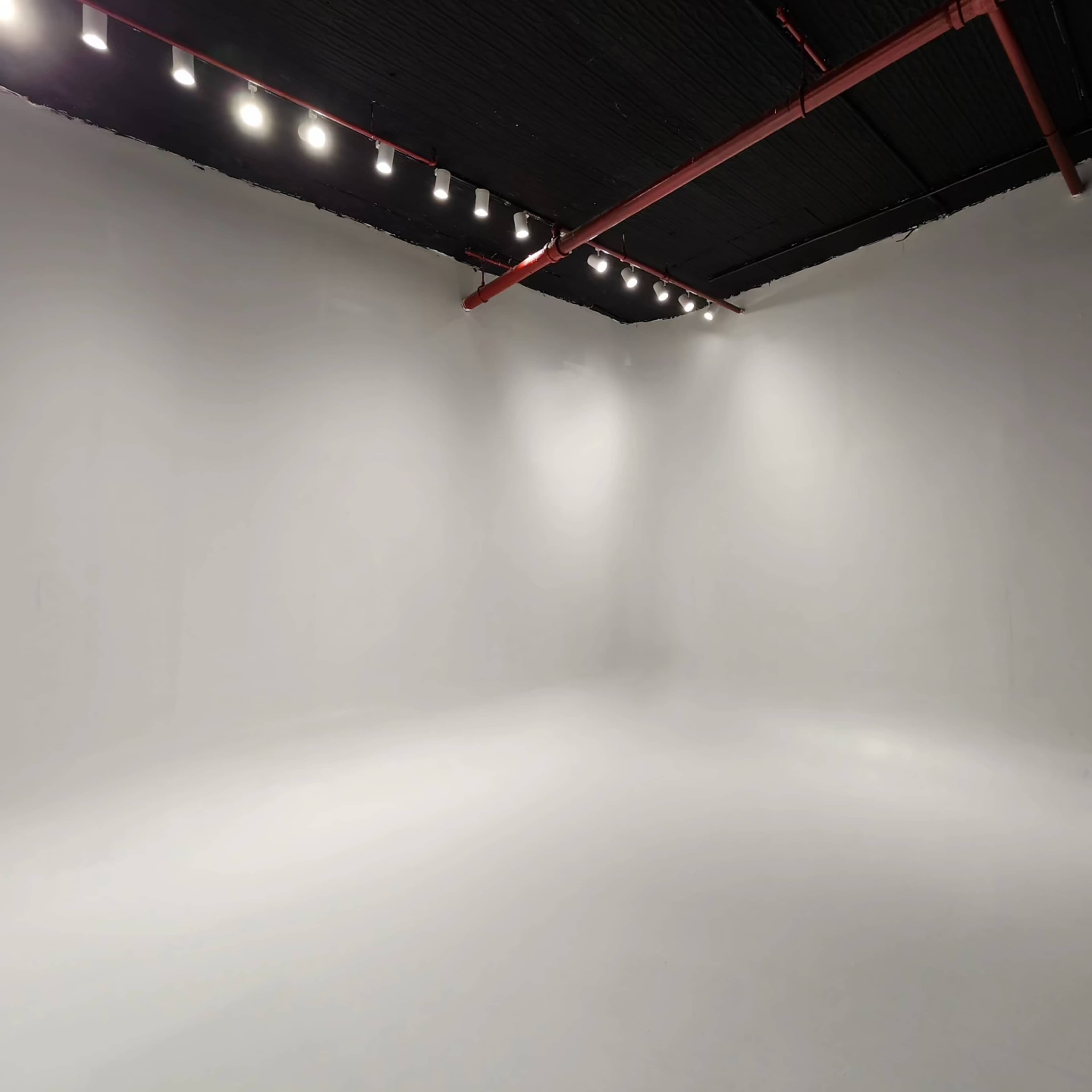 A spacious, empty studio with white walls and ceiling, illuminated by overhead lights.