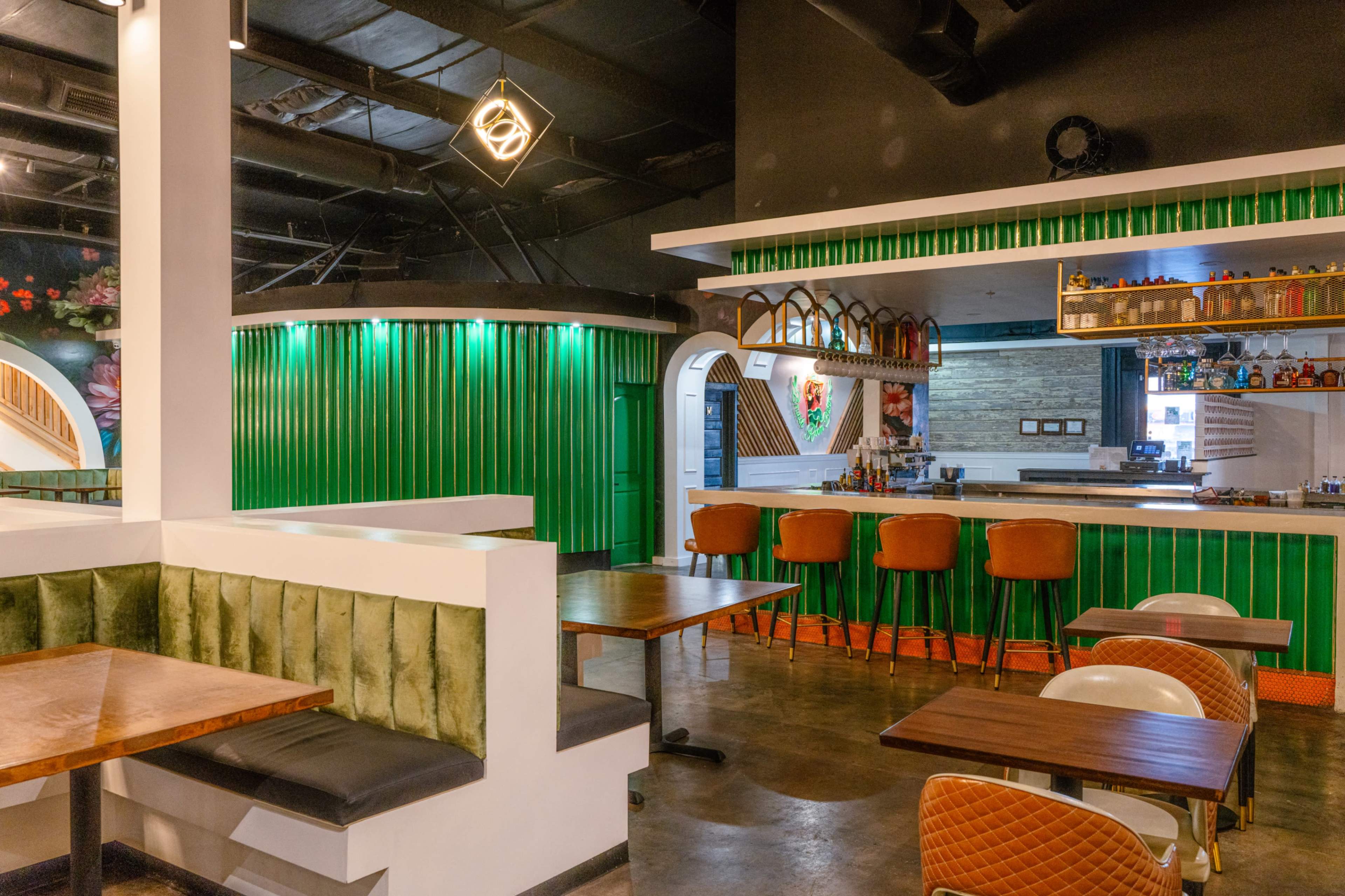 The image shows a modern restaurant interior featuring green walls, wooden tables, and various seating arrangements.