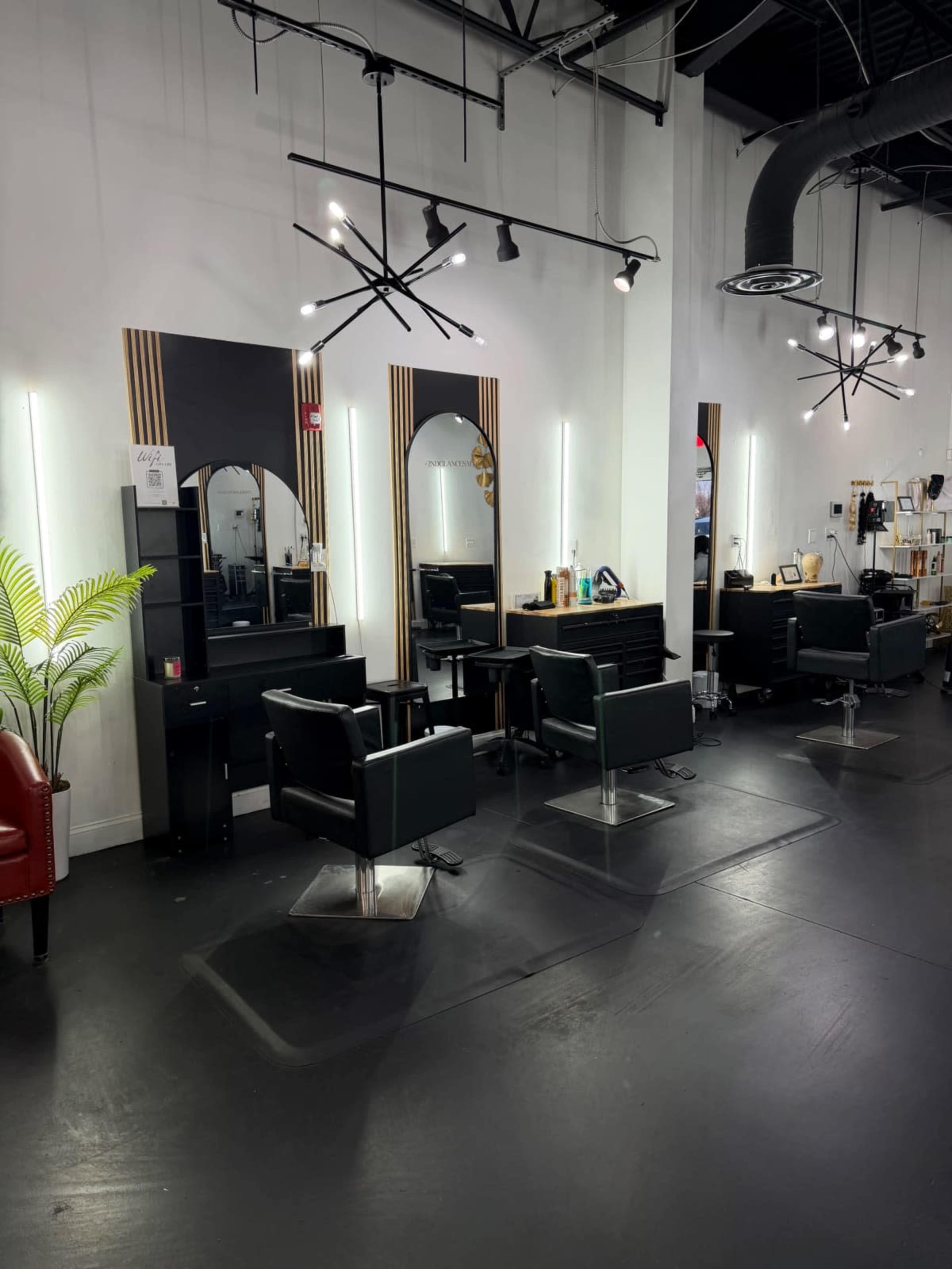 The interior of a modern hair salon features black styling chairs, illuminated mirrors, and sleek lighting fixtures against a minimalist backdrop.