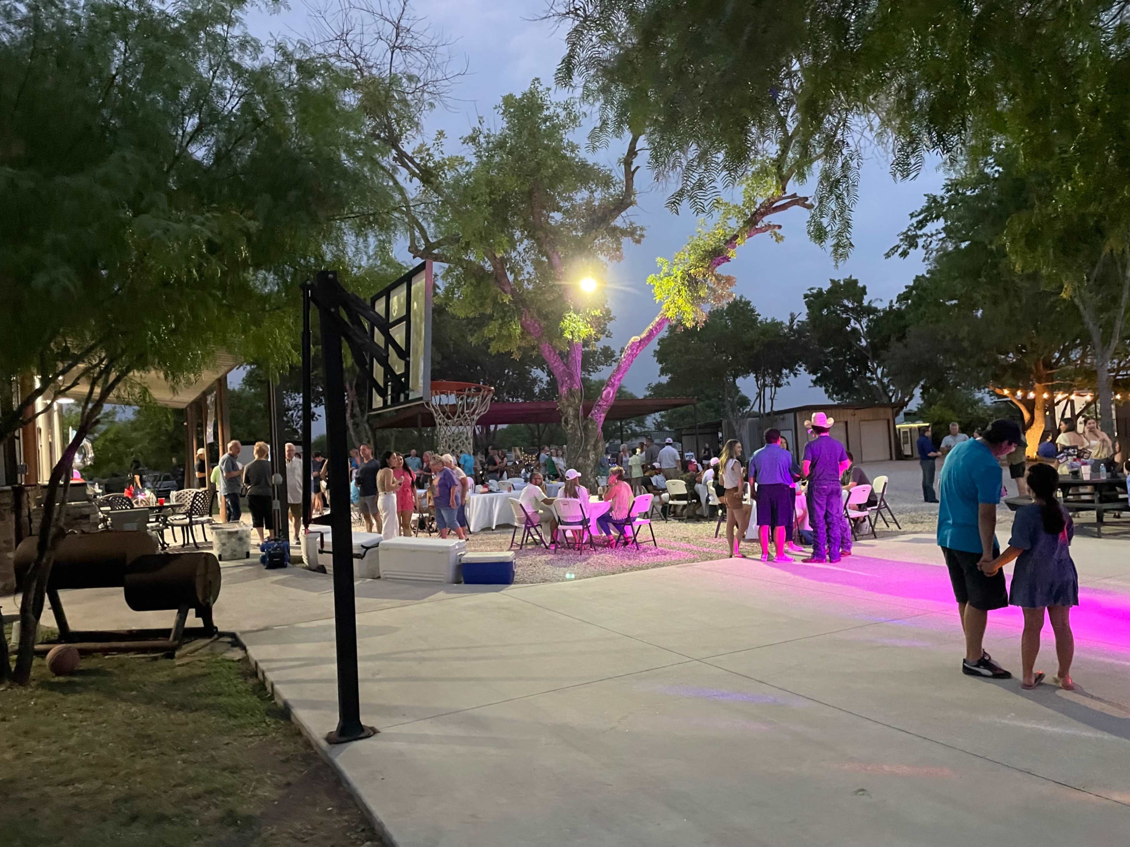 A group of people gathers for an evening event in an outdoor space decorated with chairs and lighting.