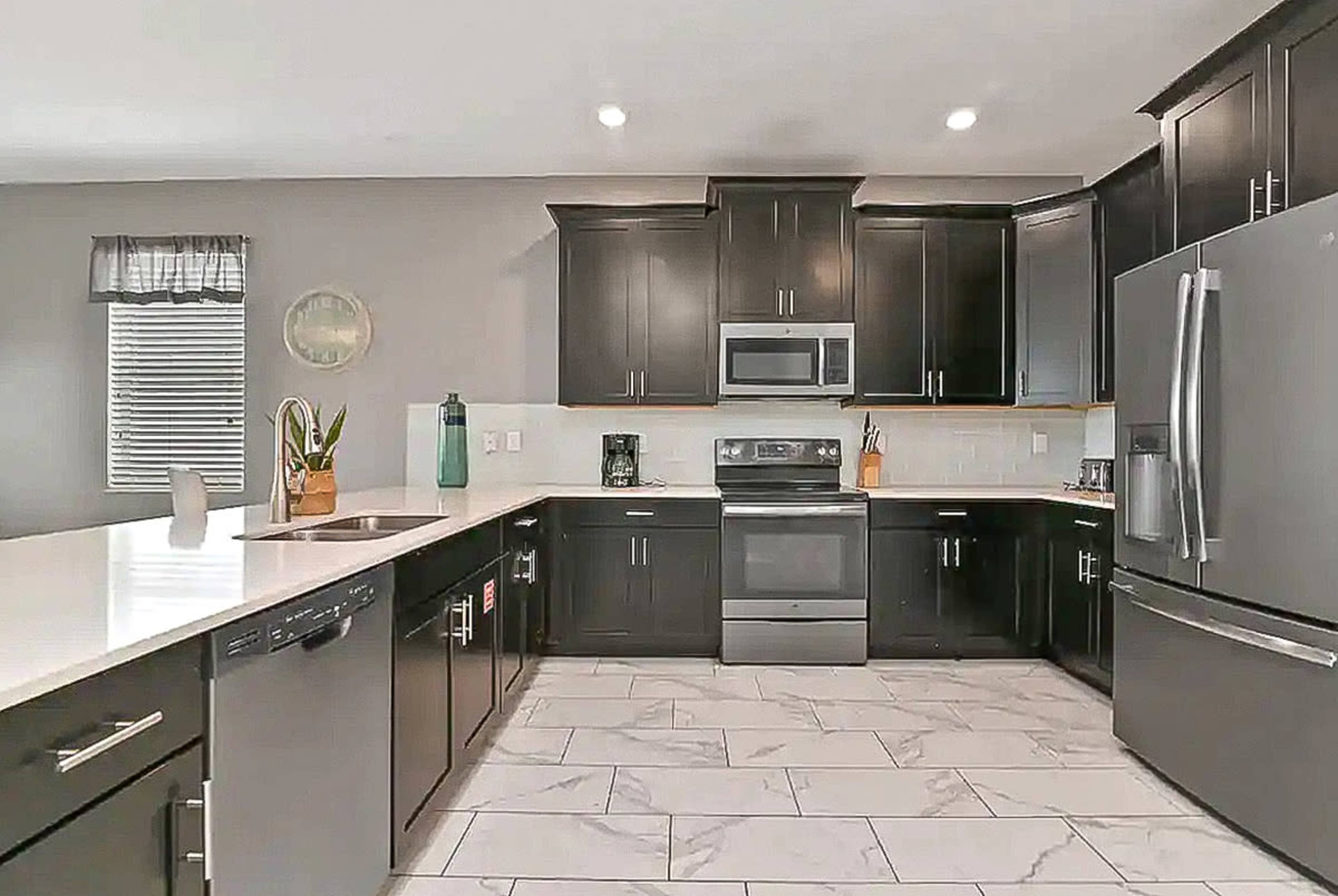 A modern kitchen with dark cabinetry, stainless steel appliances, and a light-colored countertop.
