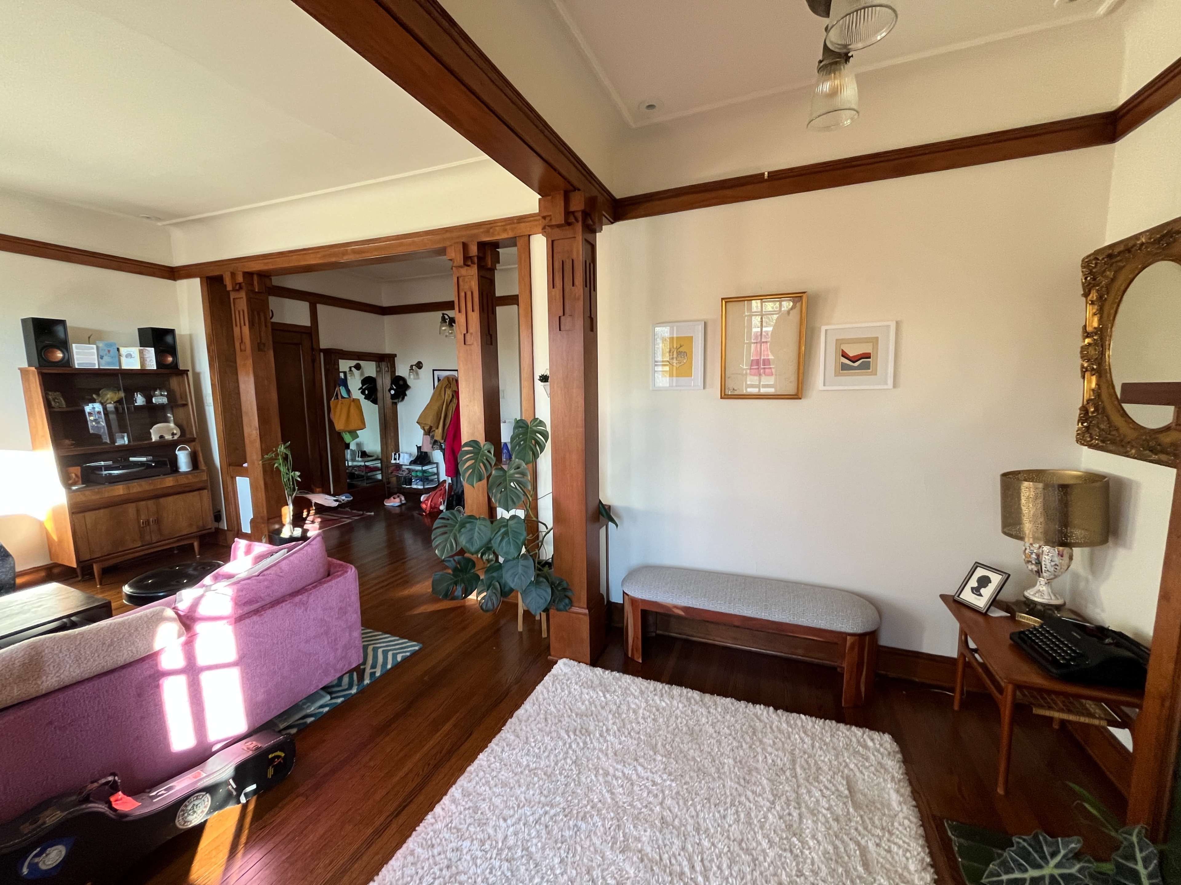 A bright living space features wooden beams, a plush area rug, a small bench, and a seating area with a purple sofa and various decorative items.