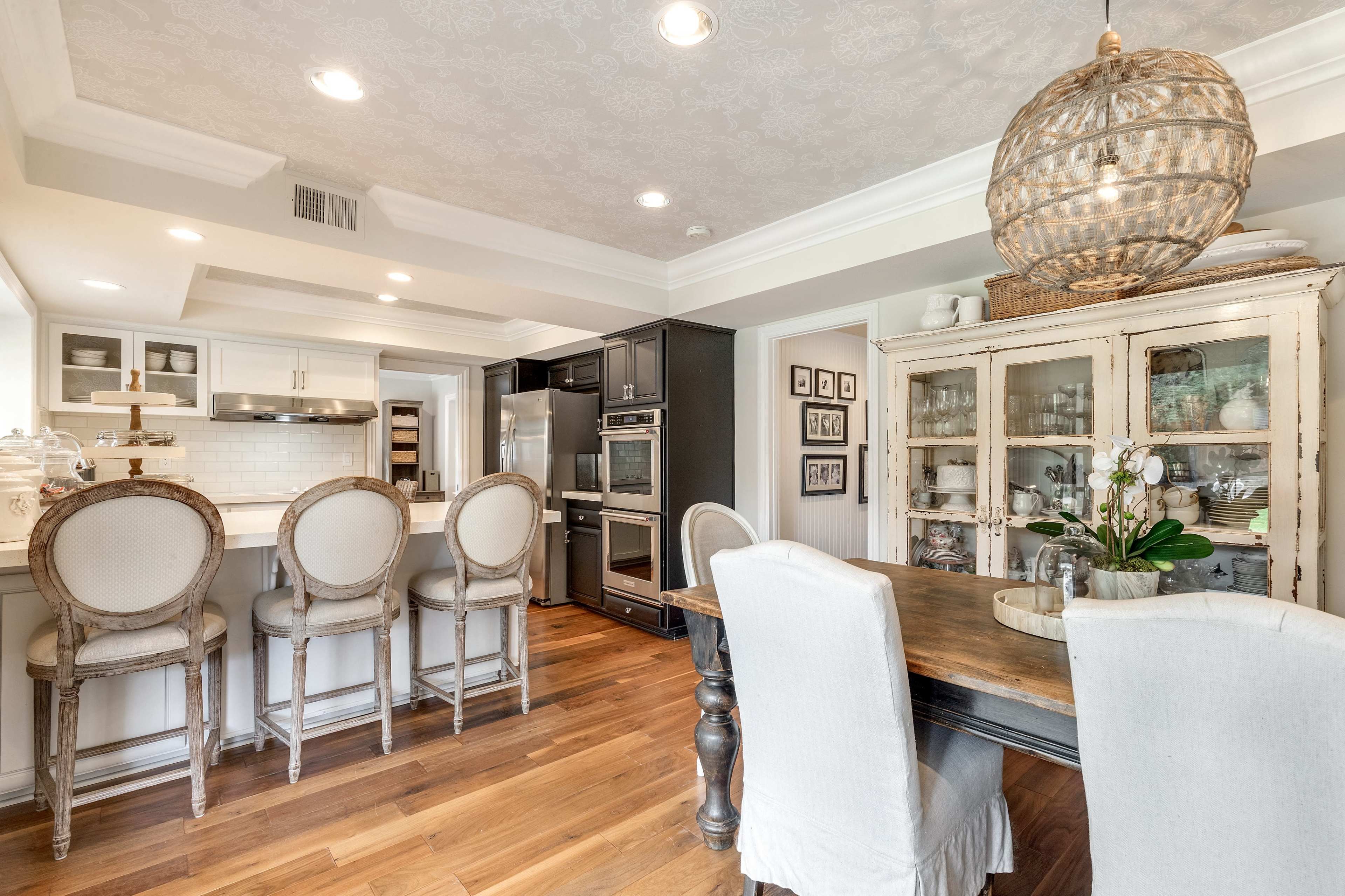 A kitchen with a wooden dining table and chairs, an island bar with stools, and appliances integrated into the cabinetry.