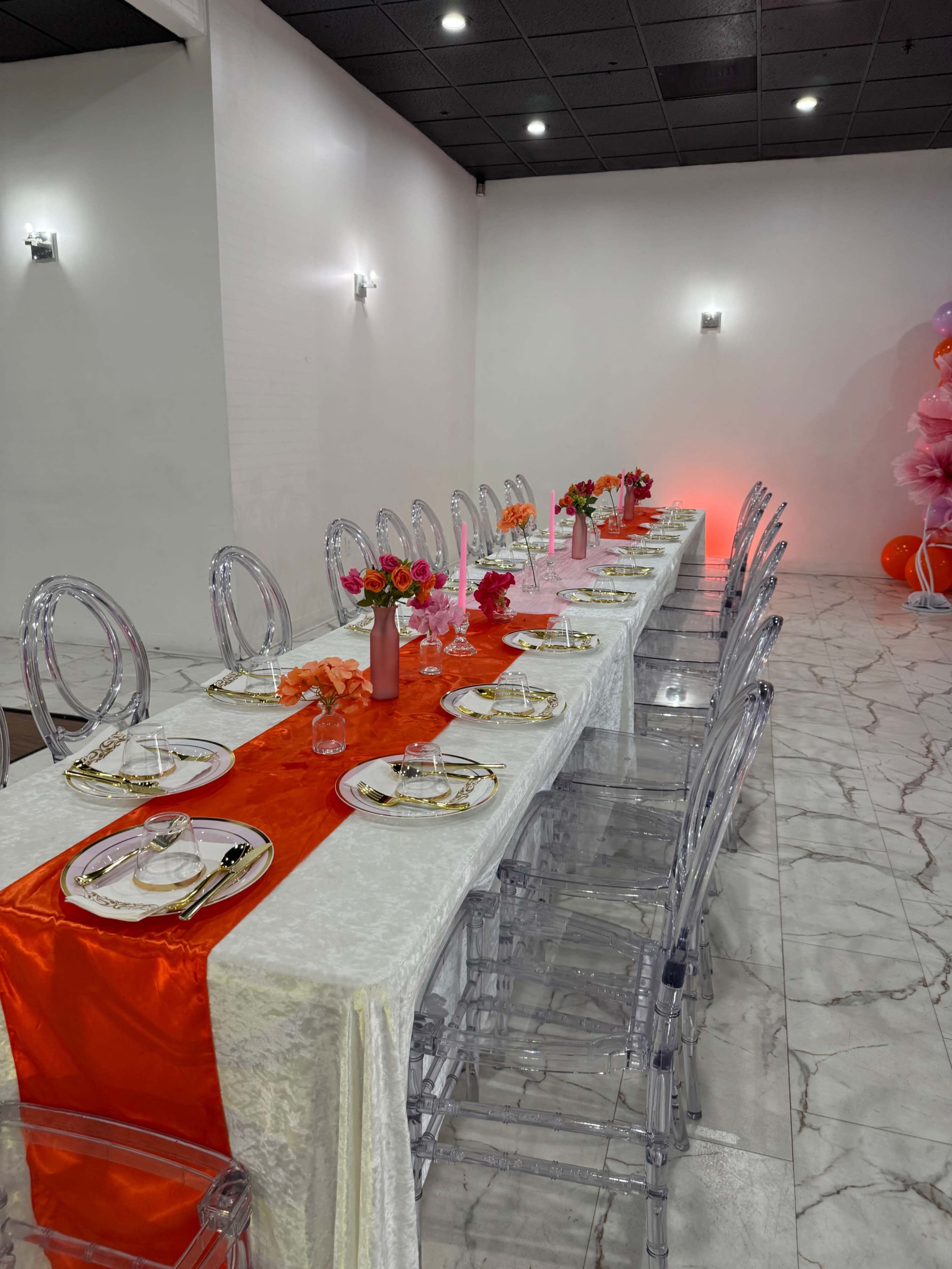 A long dining table is set with clear chairs, elegant tableware, and decorated with floral arrangements along the center.