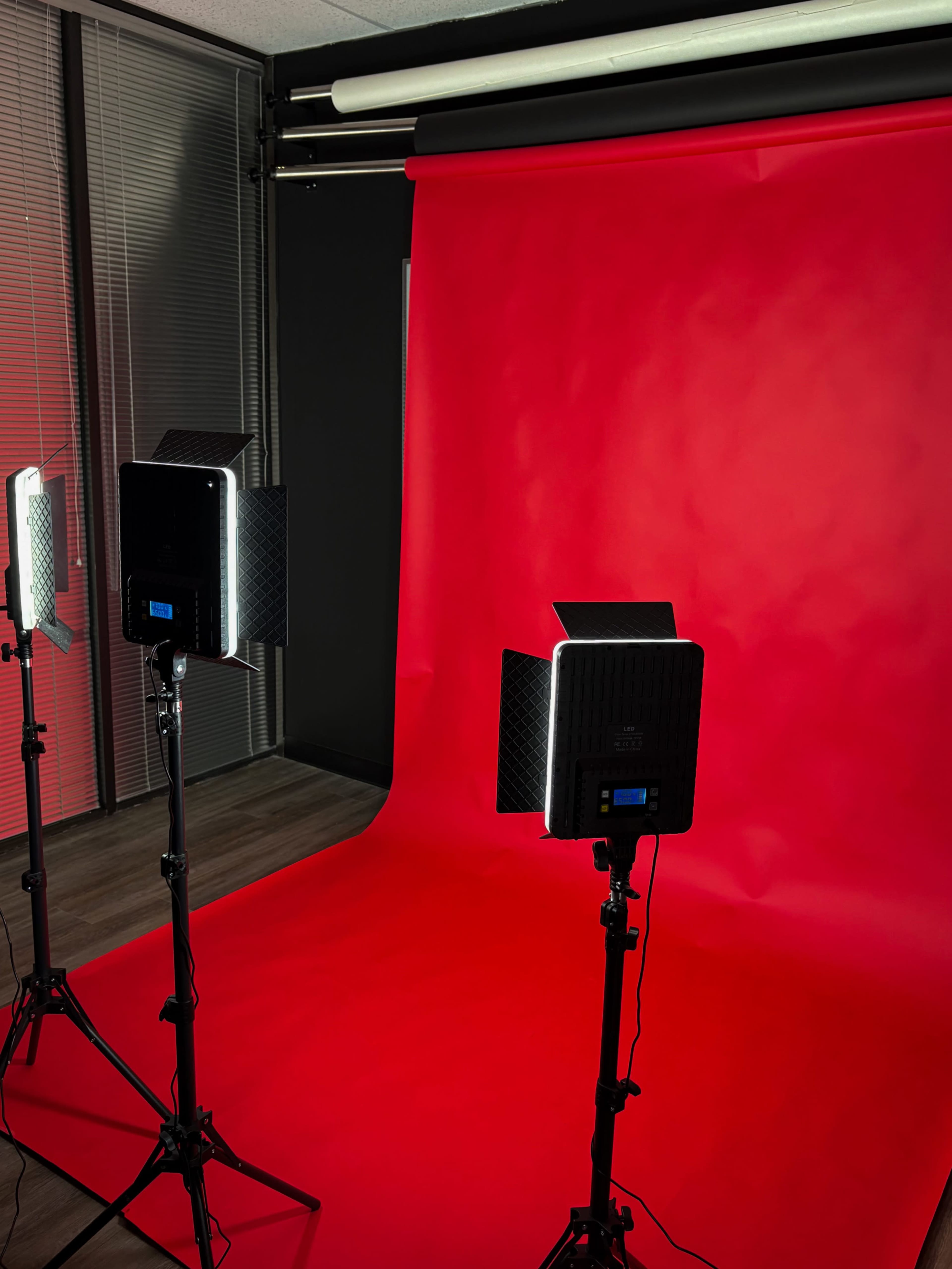 The image shows a photography setup with three lighting fixtures positioned in front of a red backdrop.