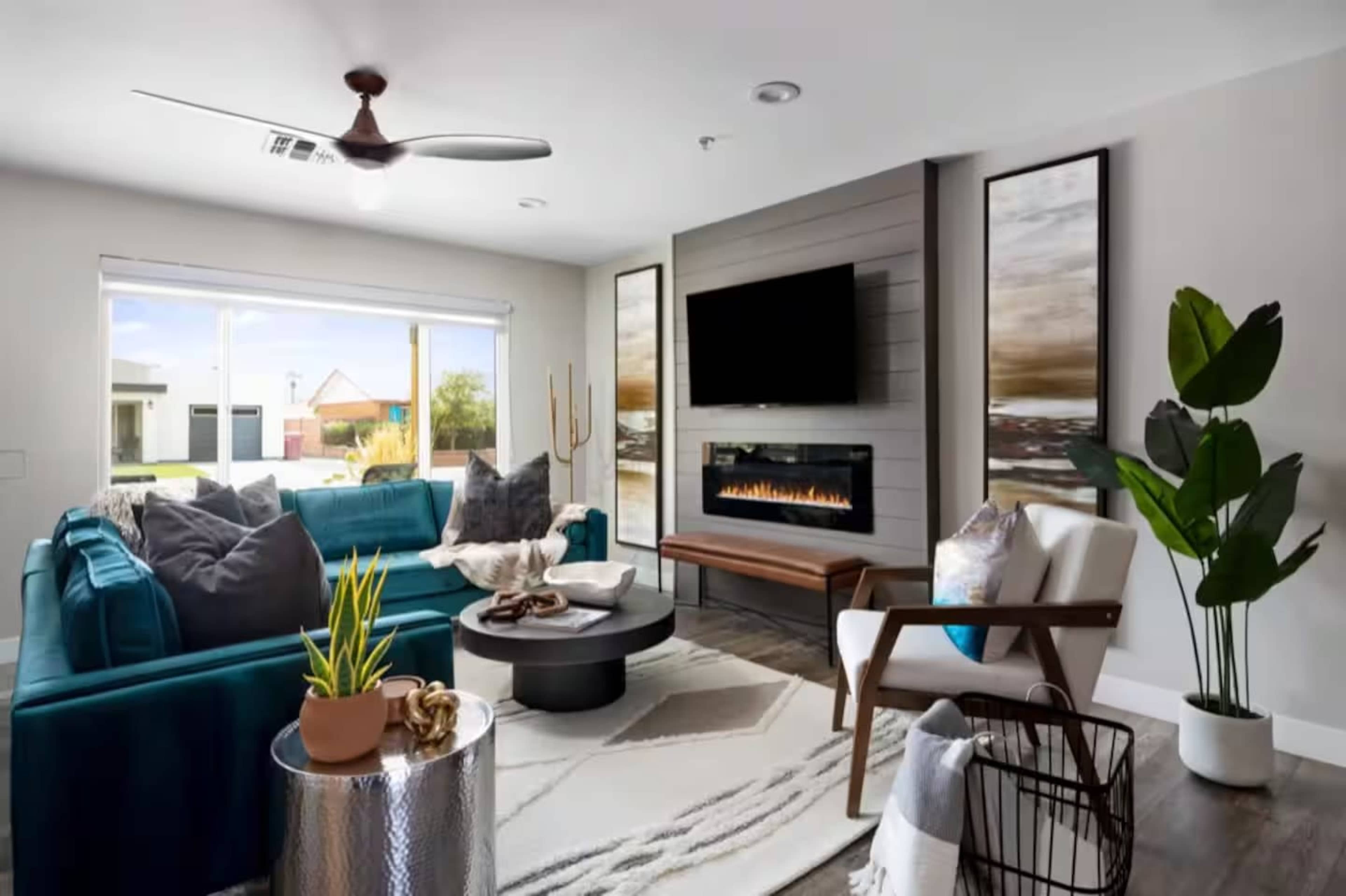 The living room features a teal sofa, a mounted television, an electric fireplace, and various decorative plants and artwork.