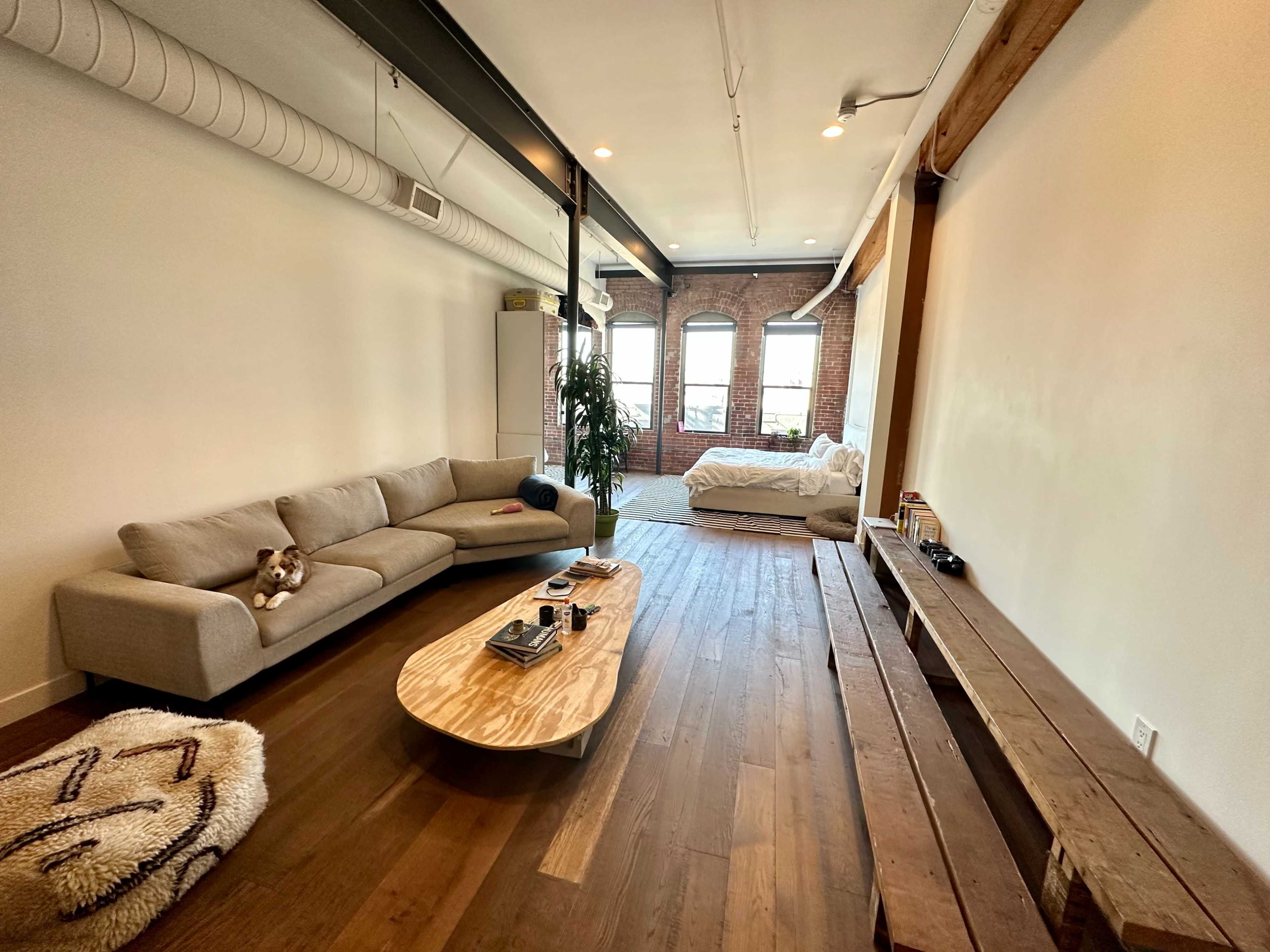 A modern living room features a light-colored sofa, a wooden coffee table, and a rustic bench, with large windows allowing natural light to fill the space.