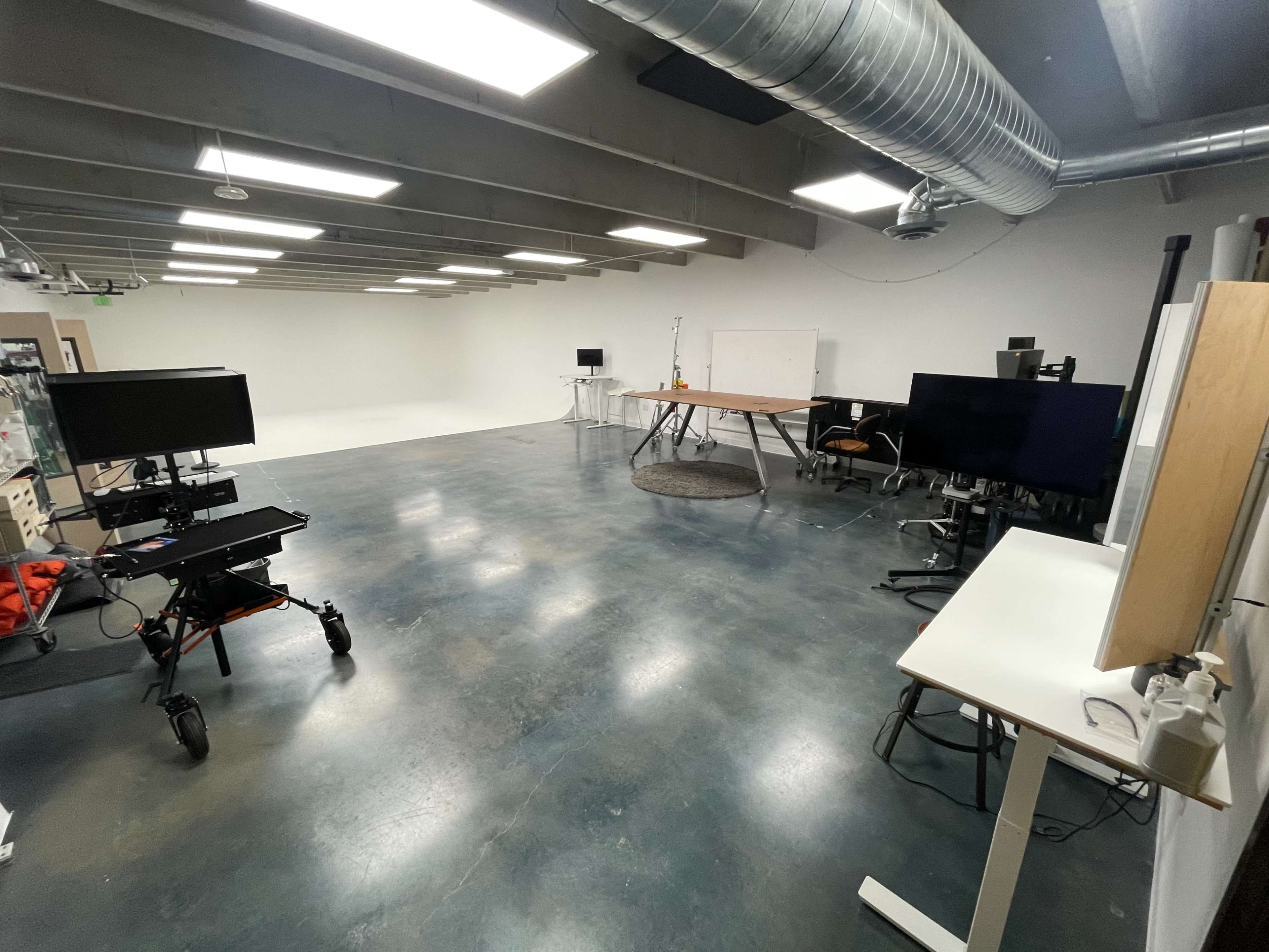 An empty, modern workspace with several desks, computers on stands, and industrial-style lighting.