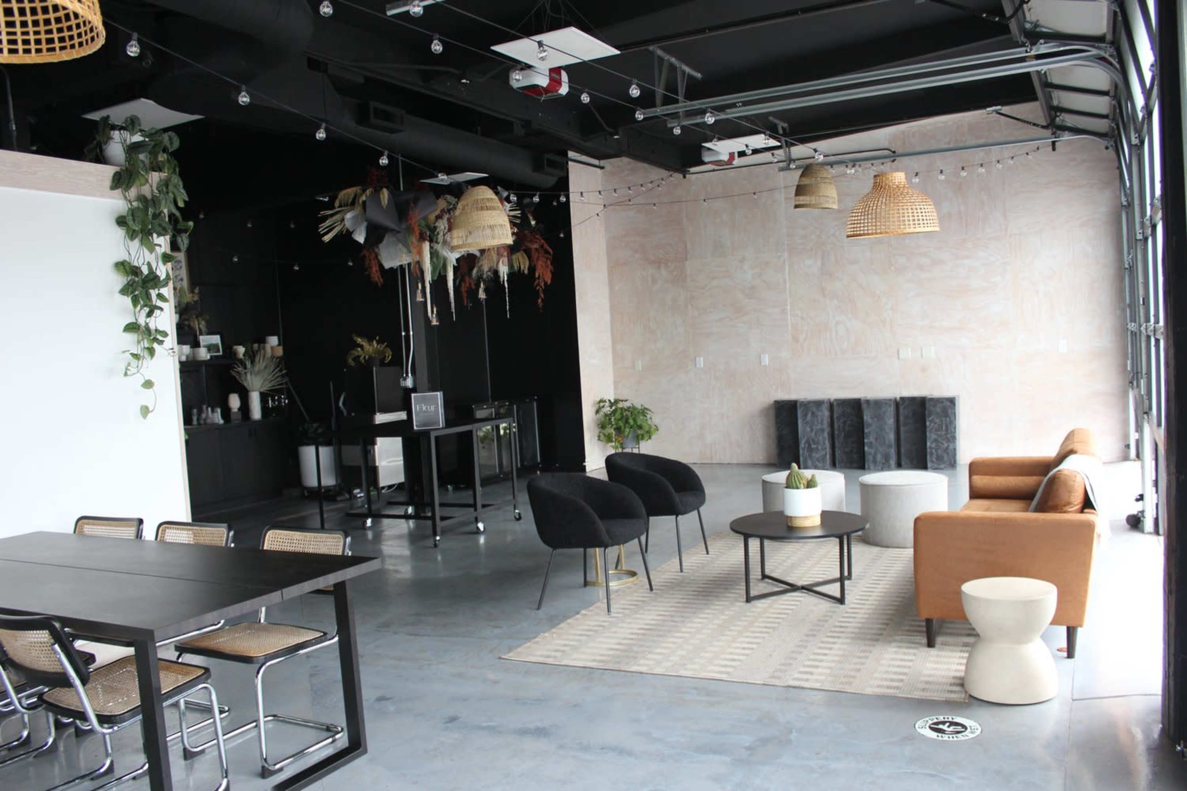 The image shows a modern interior space with a seating area featuring chairs and a table, alongside a kitchenette and decorative elements.