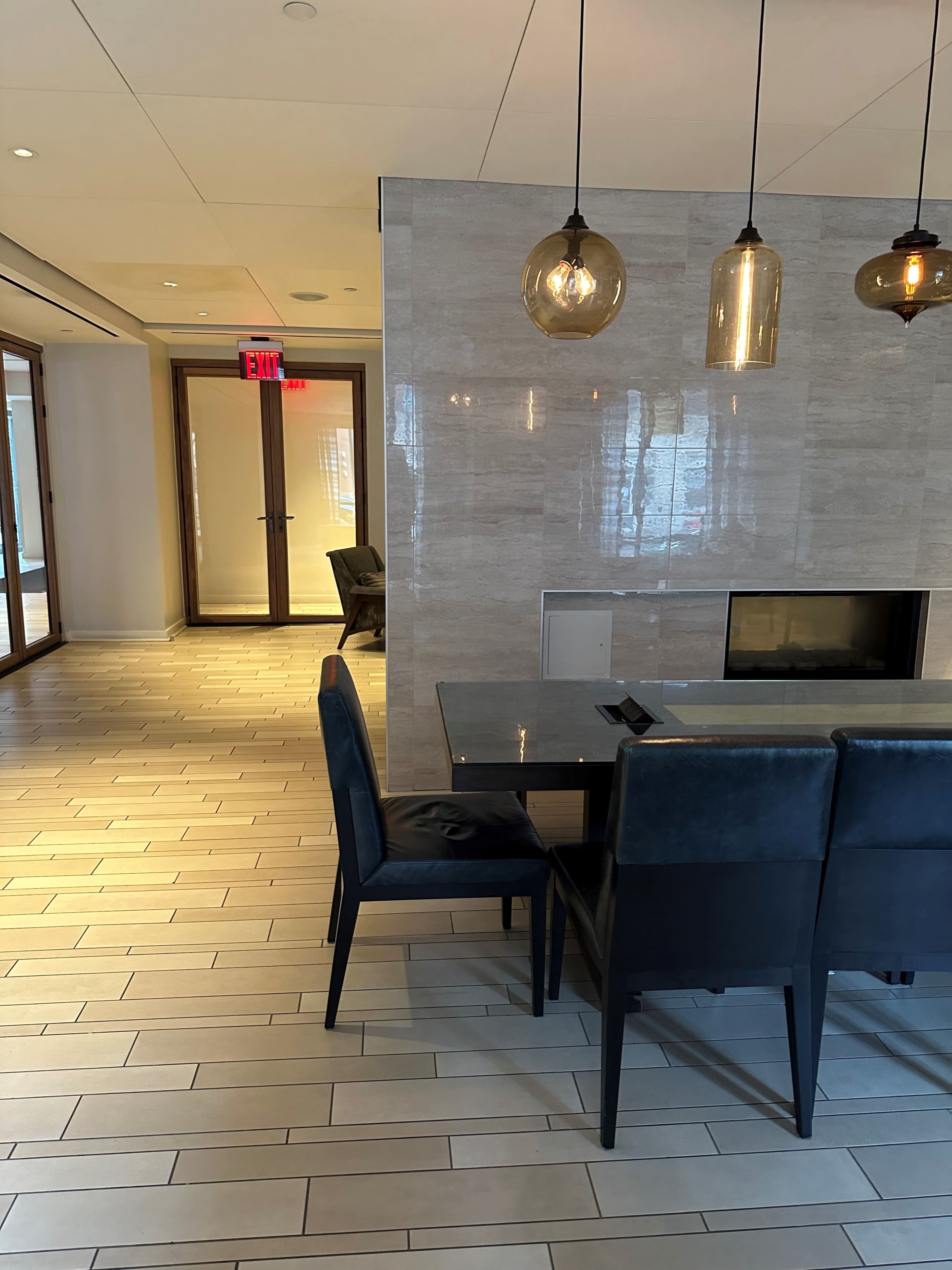The image shows a modern dining area with a dark table and chairs, leading to a hallway with glass doors and a fireplace.