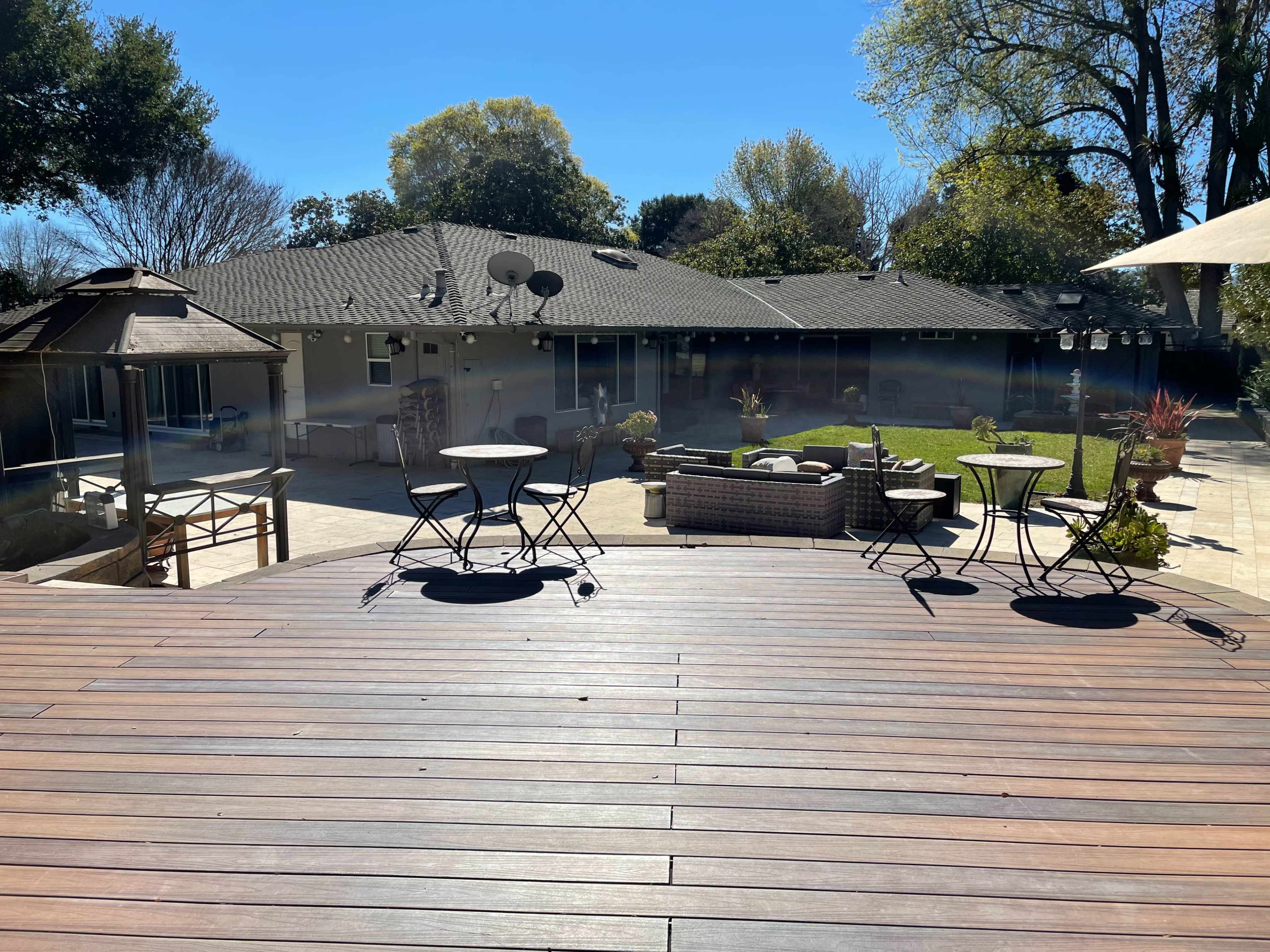 A spacious backyard with a patio, seating areas, and a lawn, surrounded by trees and a house in the background.