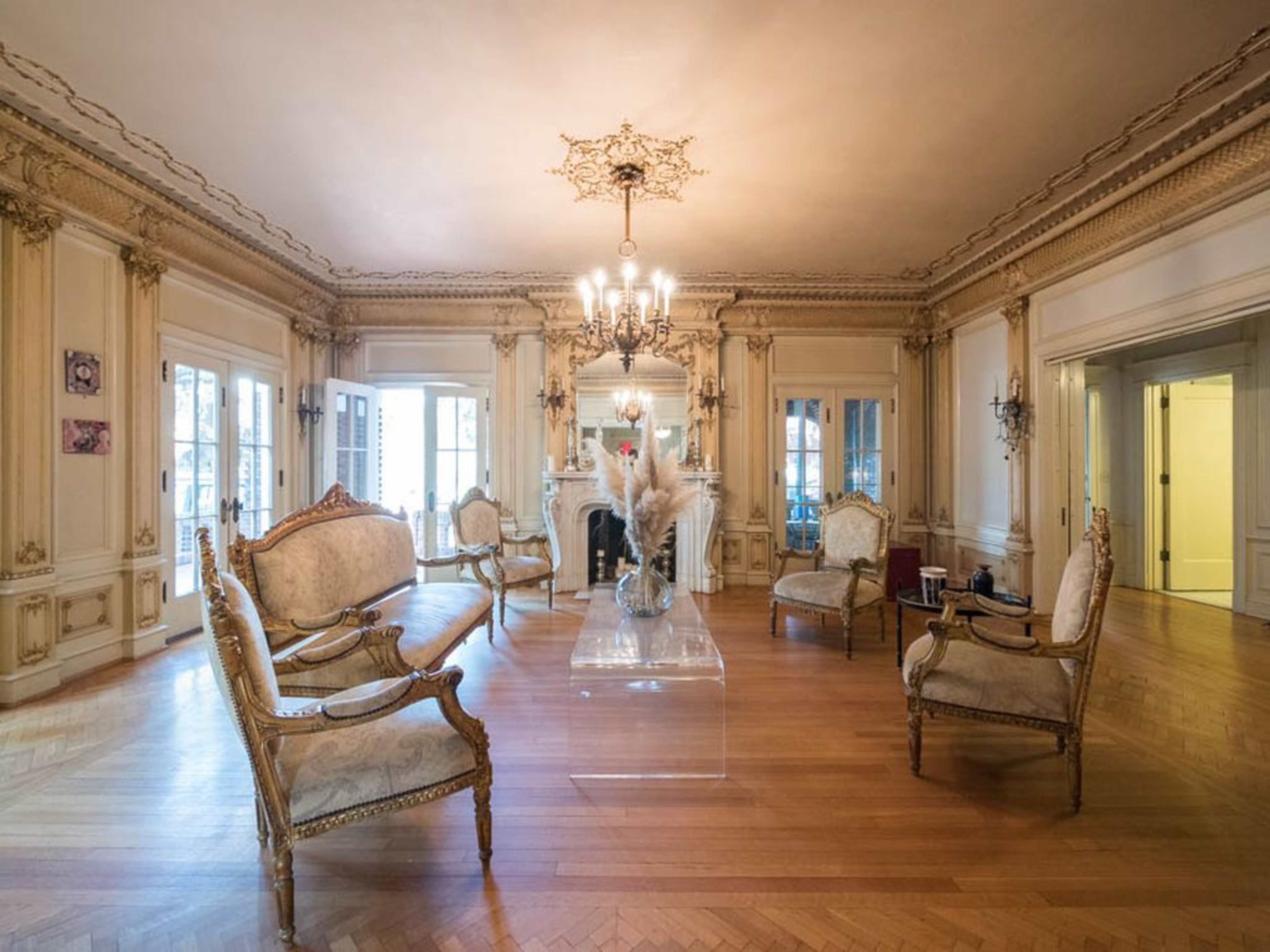 An elegantly furnished living room with ornate decor, featuring a clear glass table and several antique chairs arranged around it.