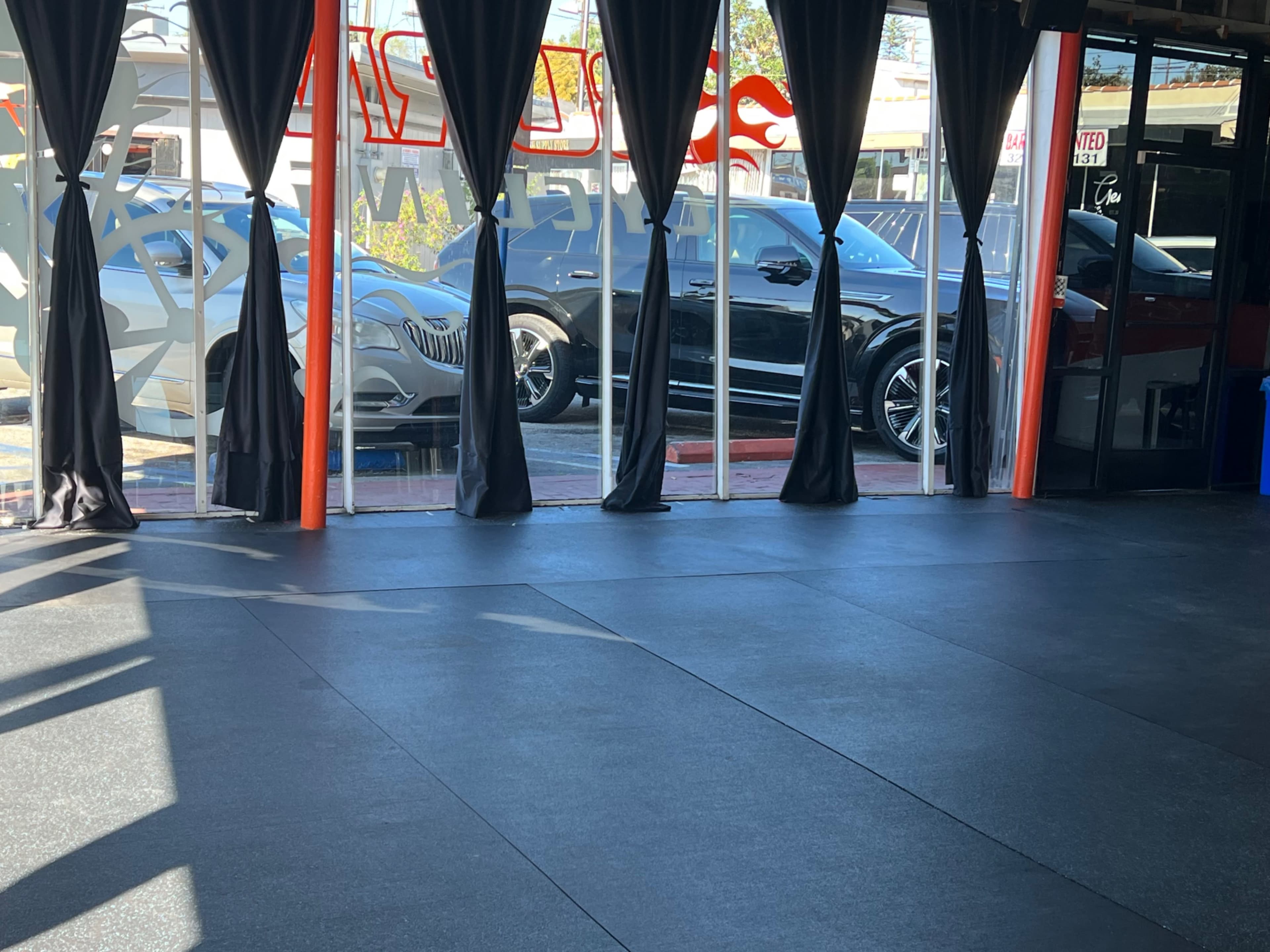 The image shows an empty gym interior with large windows displaying parked cars outside.