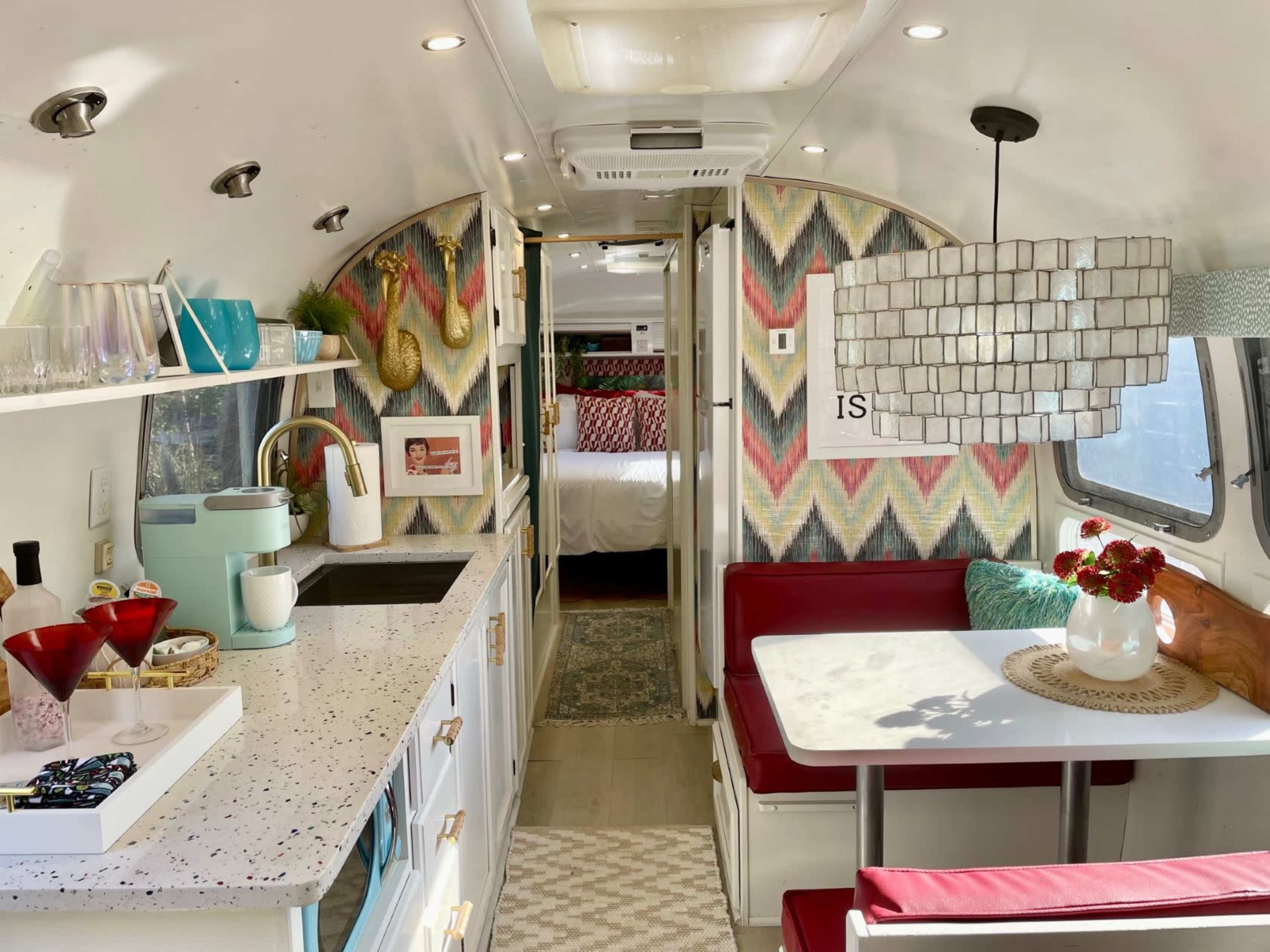 The interior of a modern, refurbished travel trailer features a compact kitchen, a dining area with a white table, and colorful patterned walls.