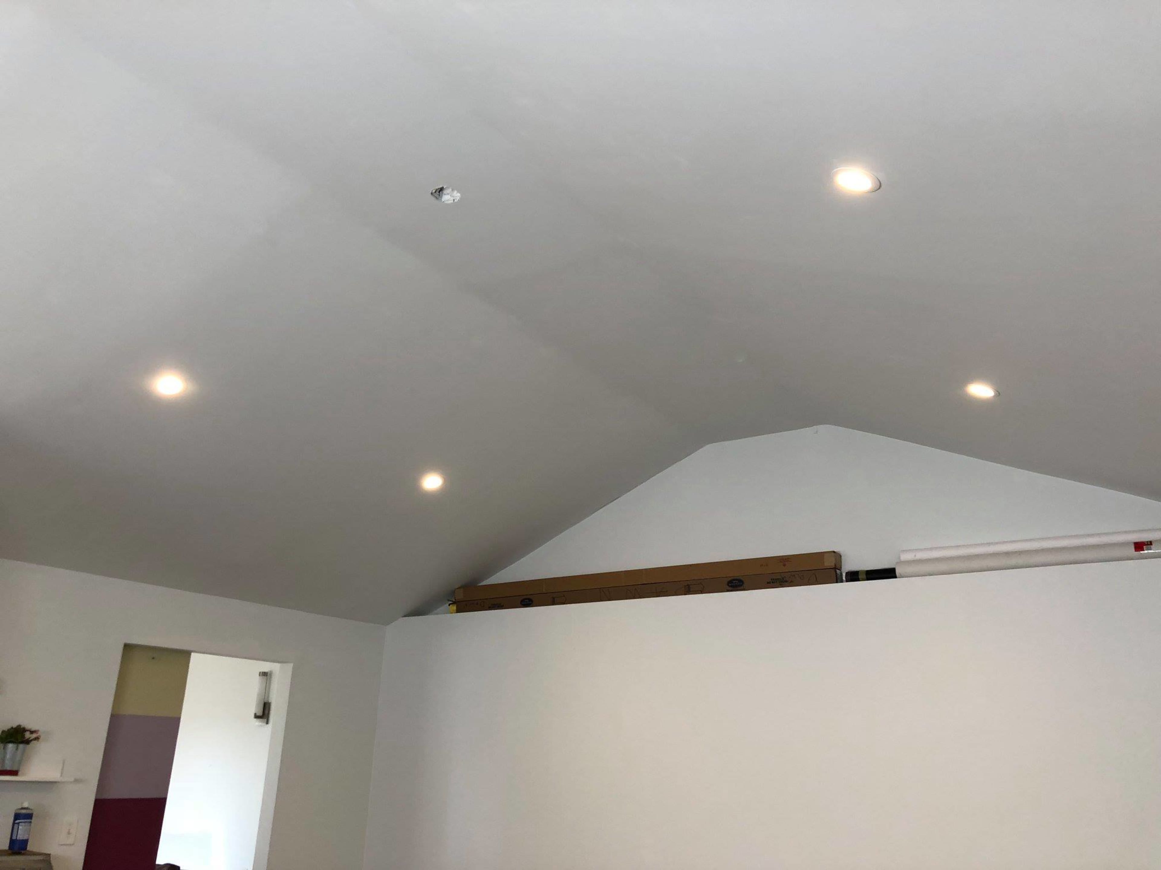 The image shows a room with a sloped ceiling, featuring recessed lighting and a partially visible wall with a door.