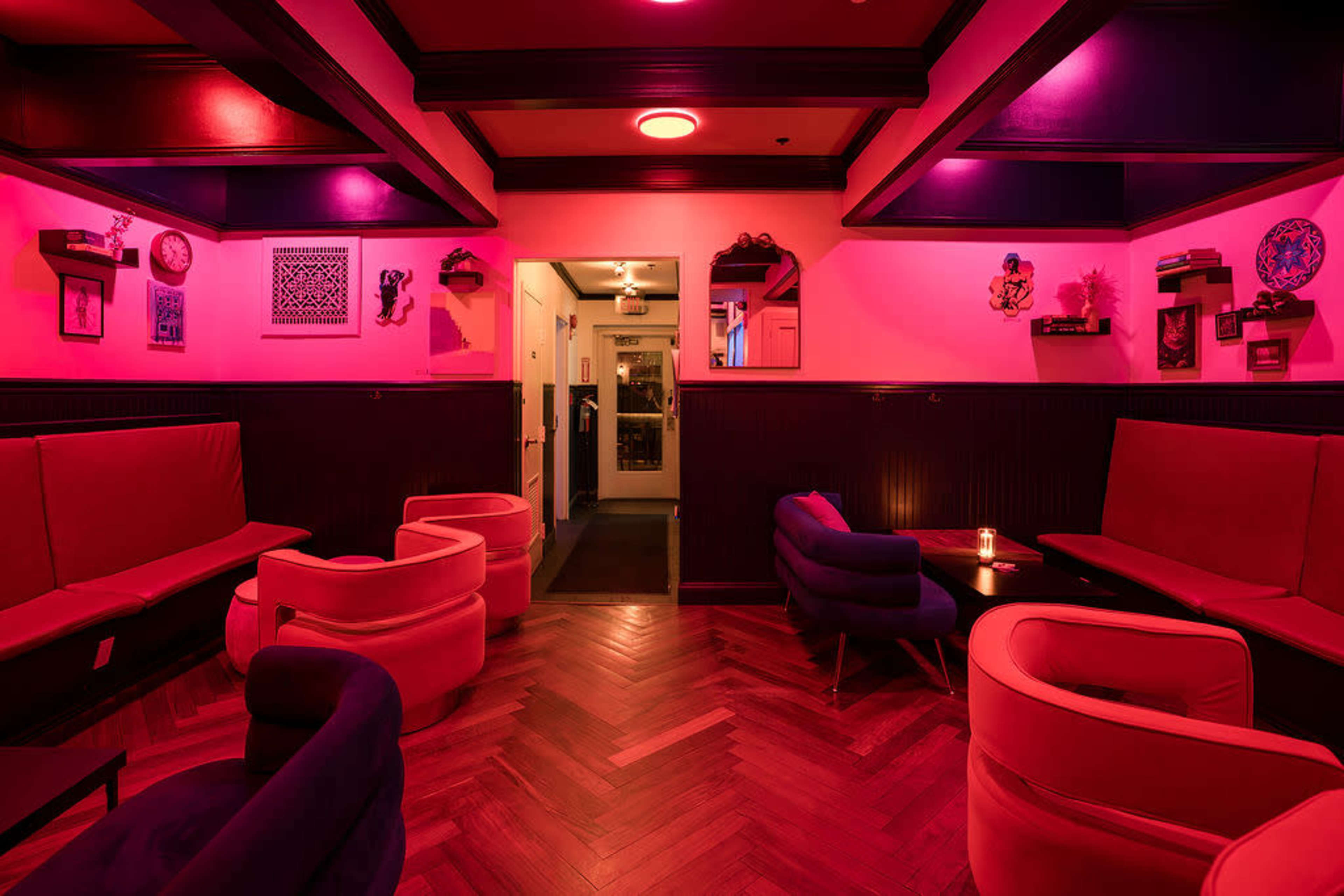 The image shows a dimly lit lounge with pink lighting, featuring modern seating and decorative wall art.
