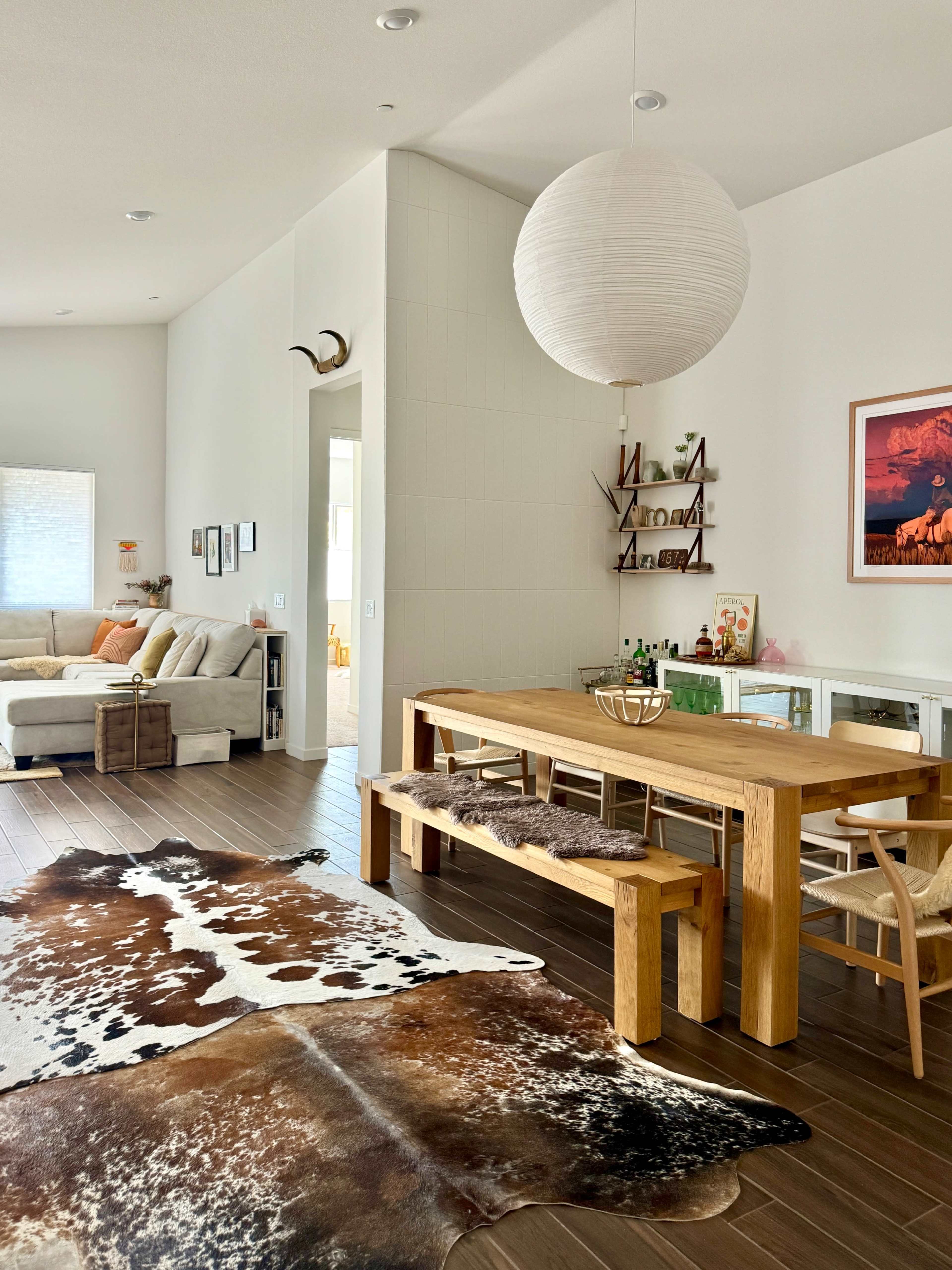 A spacious, modern living area features a wooden dining table with benches, a cowhide rug on the floor, and a cozy seating arrangement in the background.