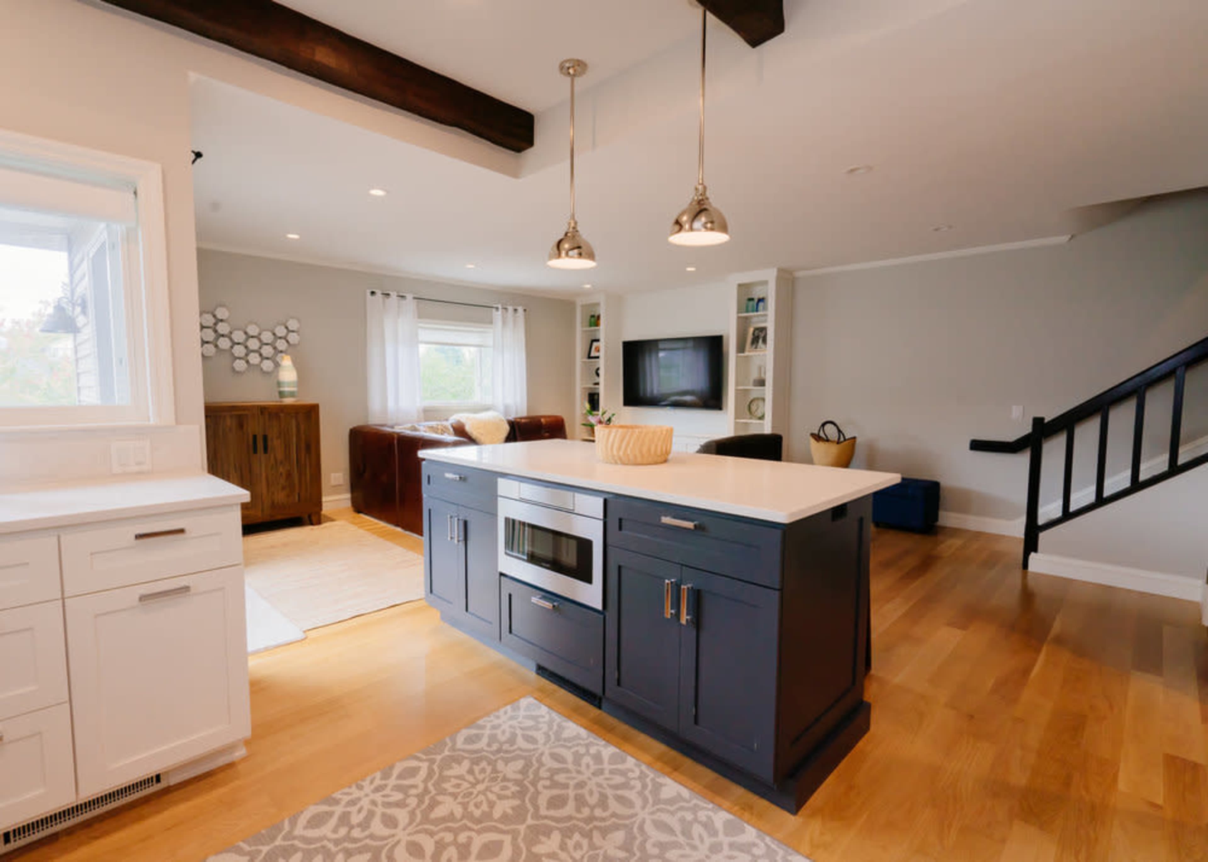 A modern kitchen with a central island, pendant lights, and an open layout leading to a living area with a sofa and television.