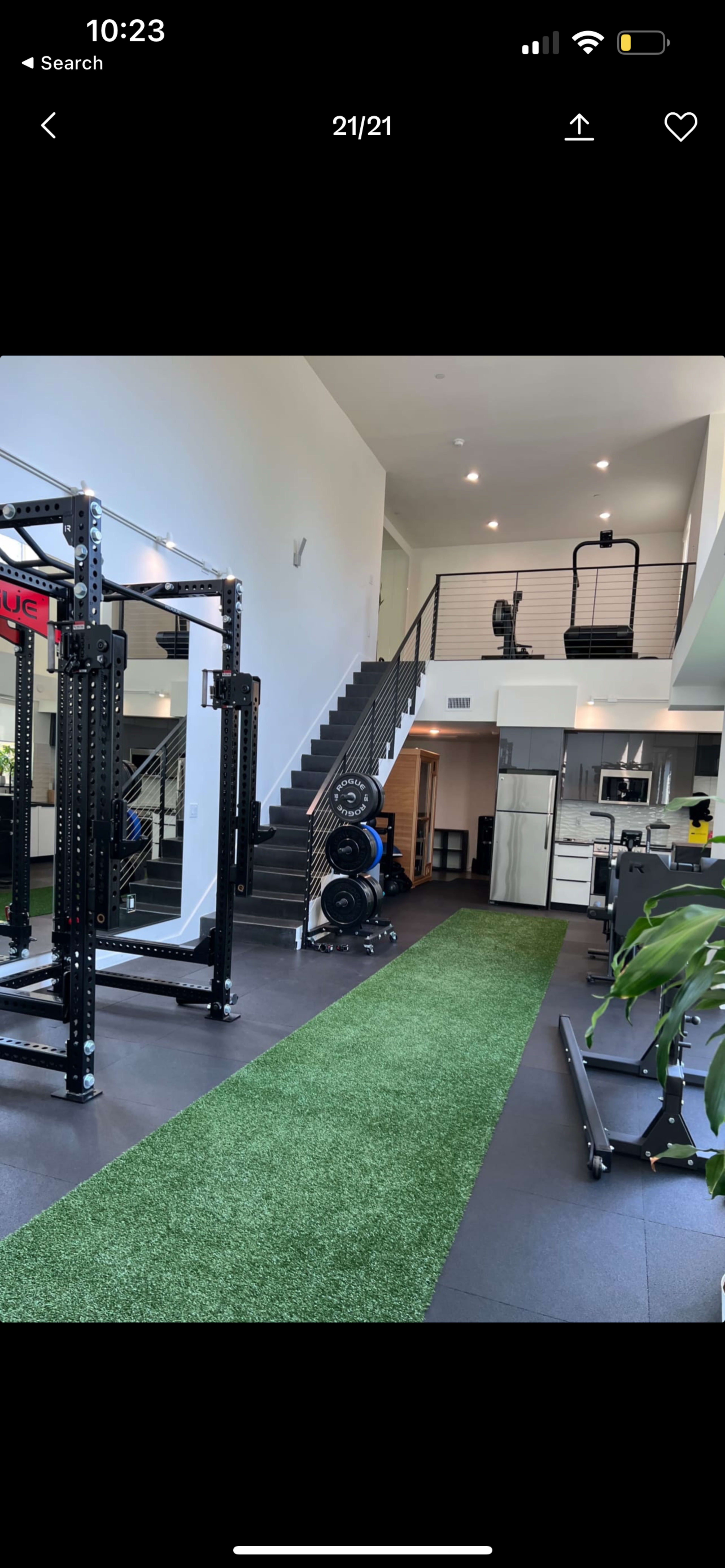 A spacious gym area with workout equipment, a staircase leading to an upper level, and artificial grass flooring.
