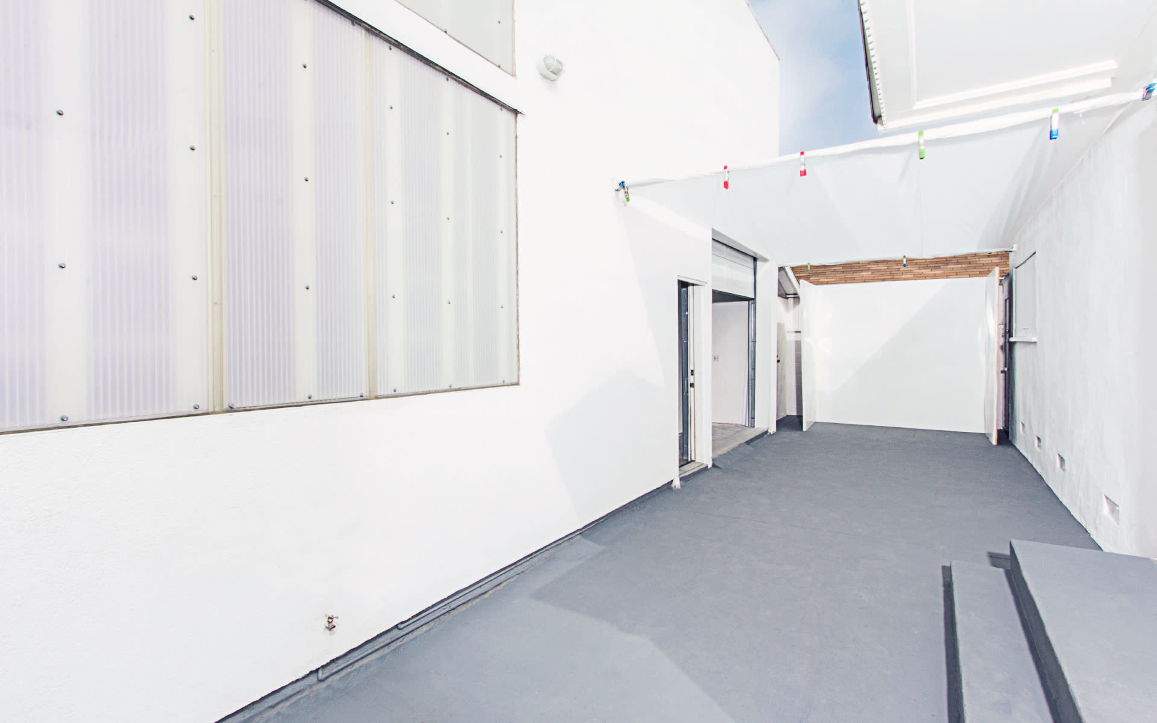 A brightly lit, minimalist outdoor space with white walls and a grey floor.