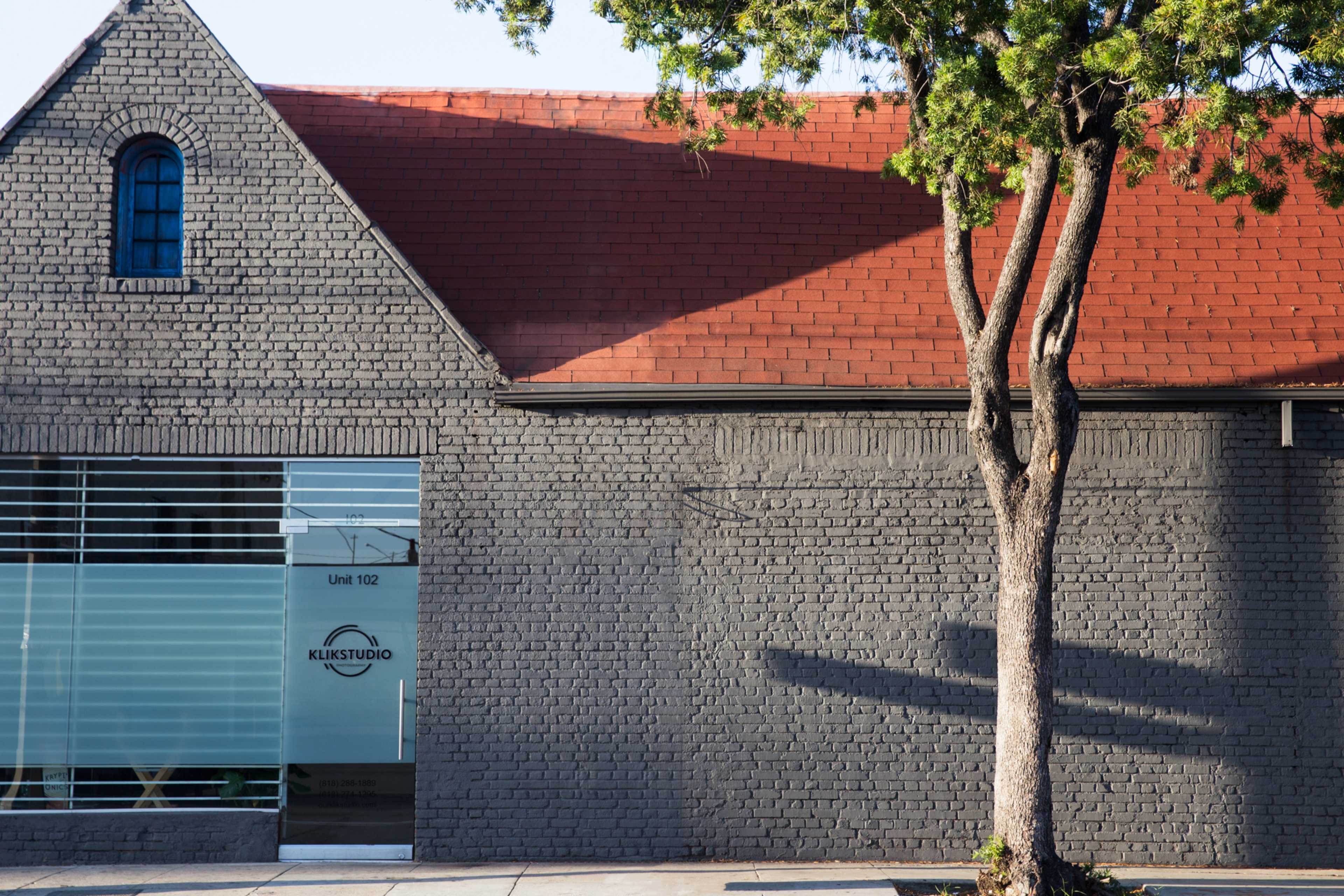 A brick building with a red-tiled roof and a glass entrance displaying the name "KLIKSTUDIO."