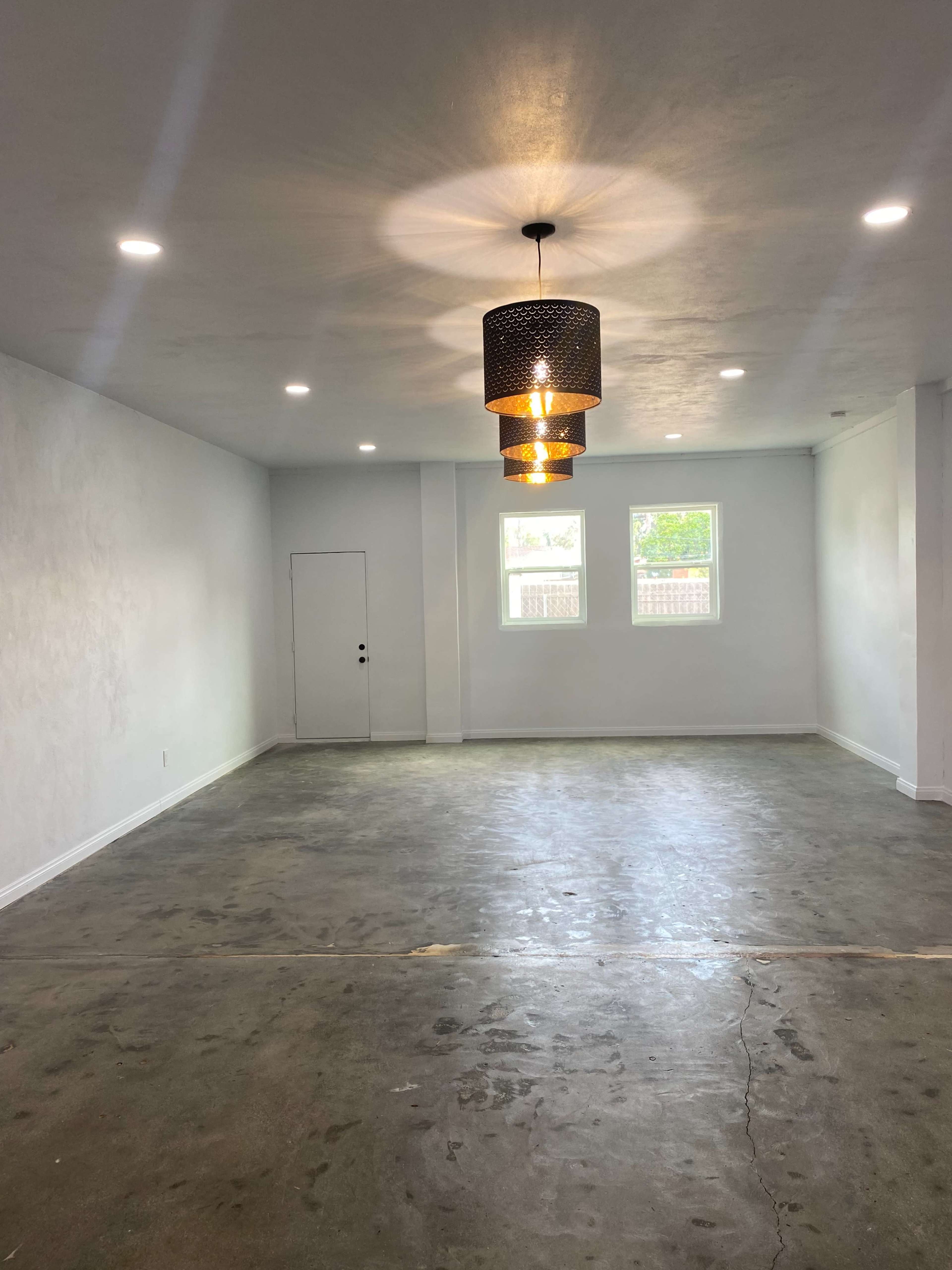 The image shows an empty room with a concrete floor, white walls, and a decorative pendant light hanging from the ceiling.